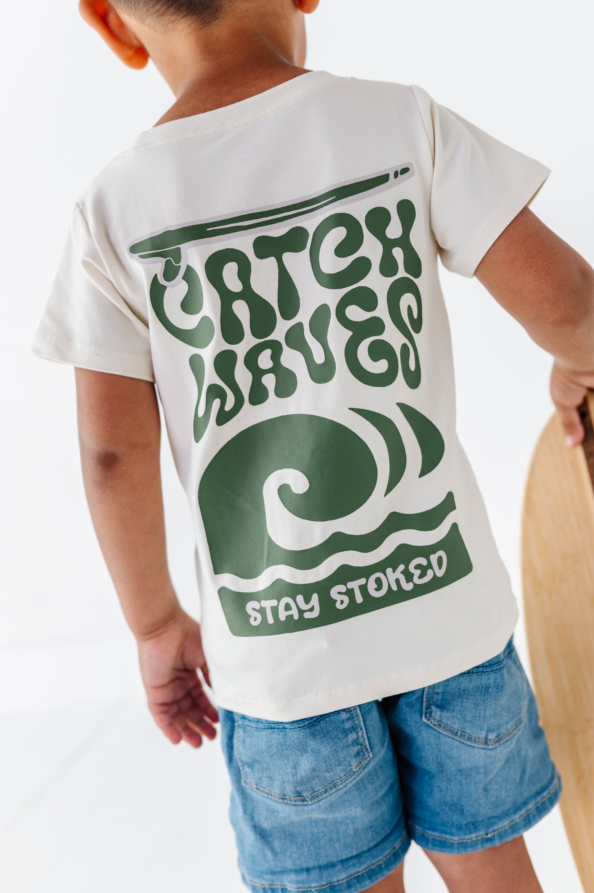 Child wearing a white t-shirt with green graphics and text on a plain background