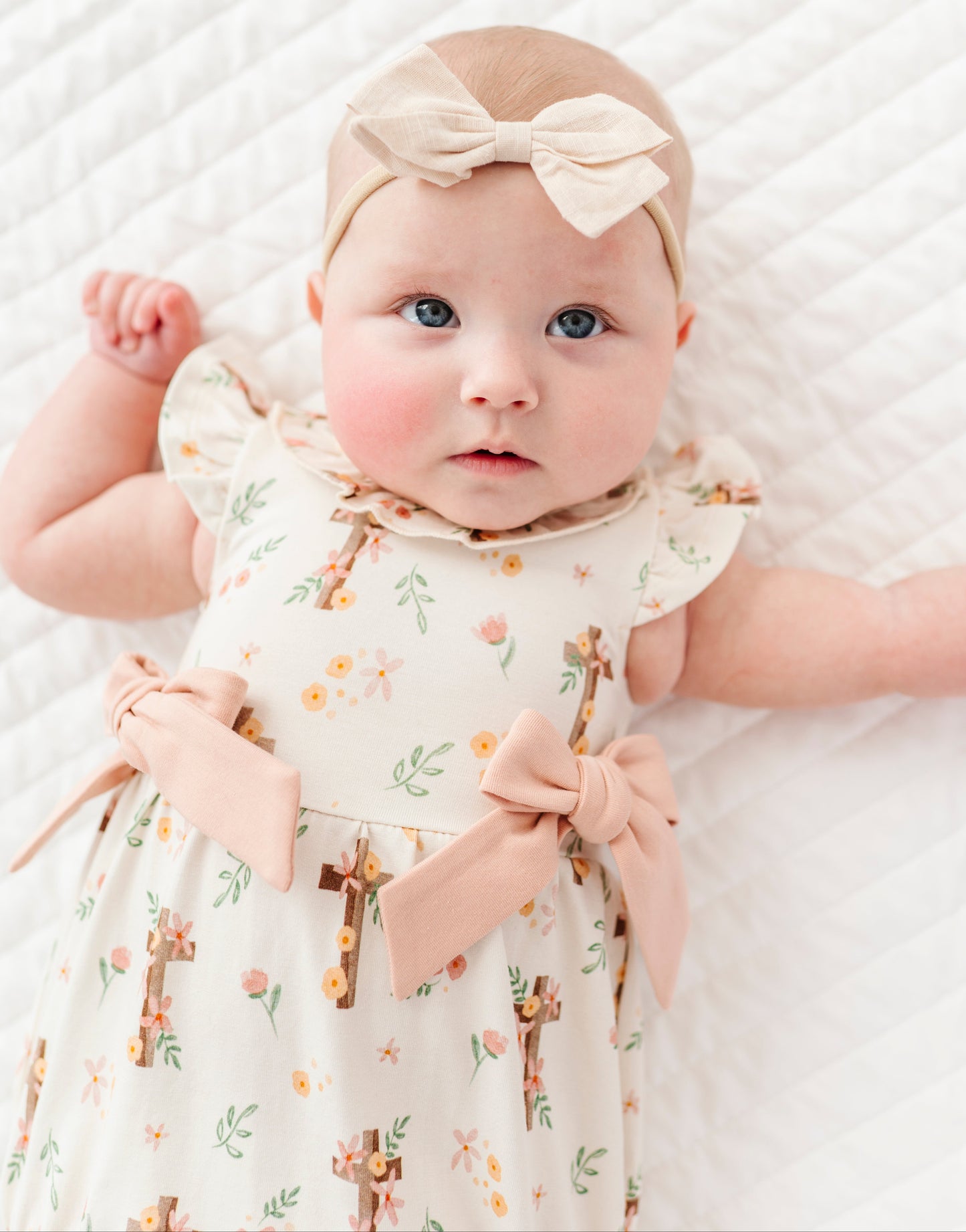 baby girl in a cross with florals bubble romper and a neutral colored headband on a white background 