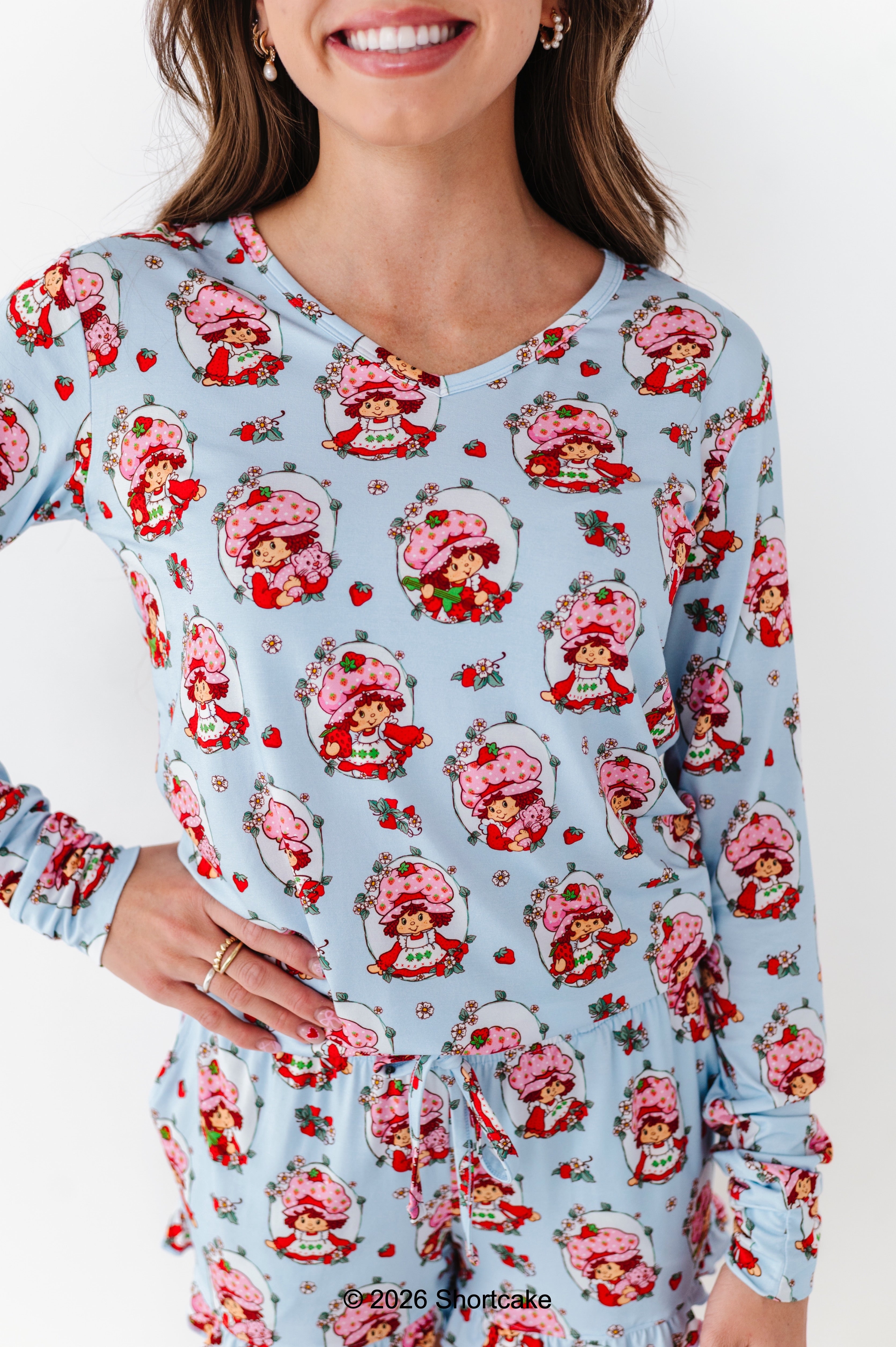 Woman wearing a light blue Strawberry Shortcake™ pajama set on a white background