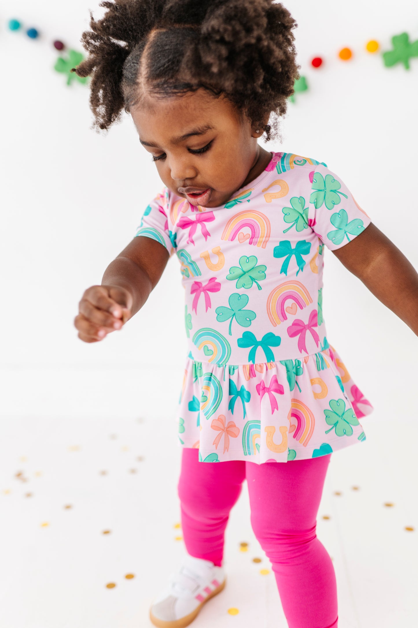Child wearing a bamboo cotton peplum top with bows and rainbows on a white background