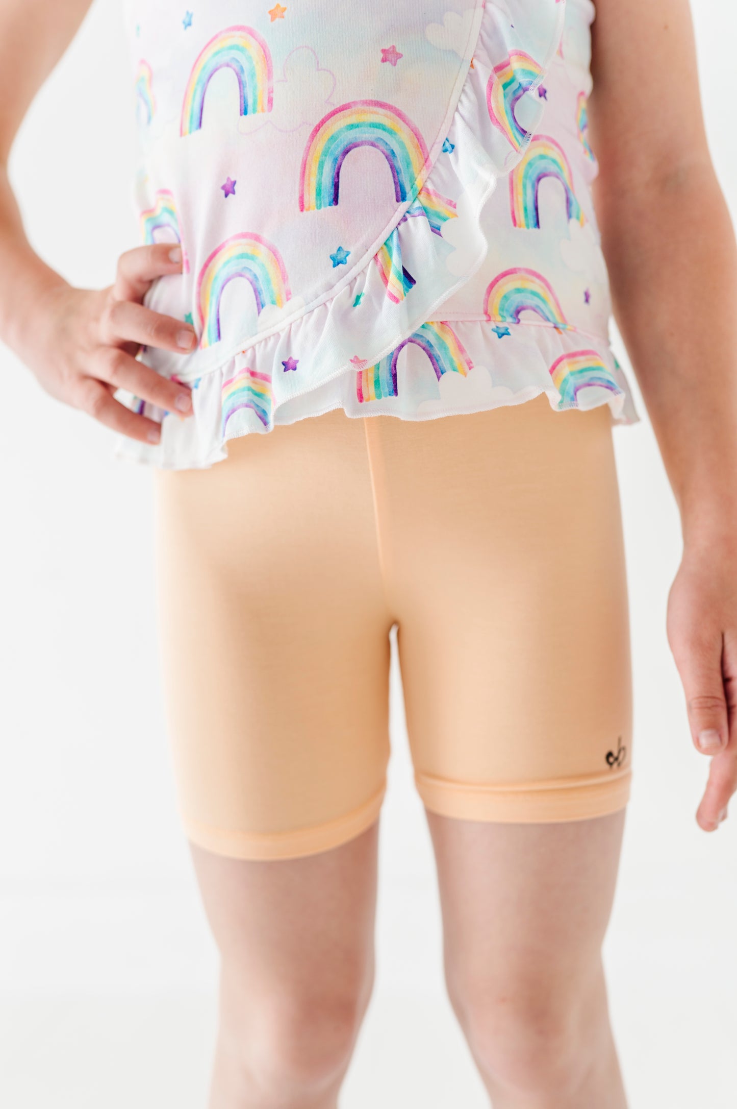 Child wearing a bamboo cotton peplum top with watercolor rainbow patterns and peach bamboo biker shorts on a white background