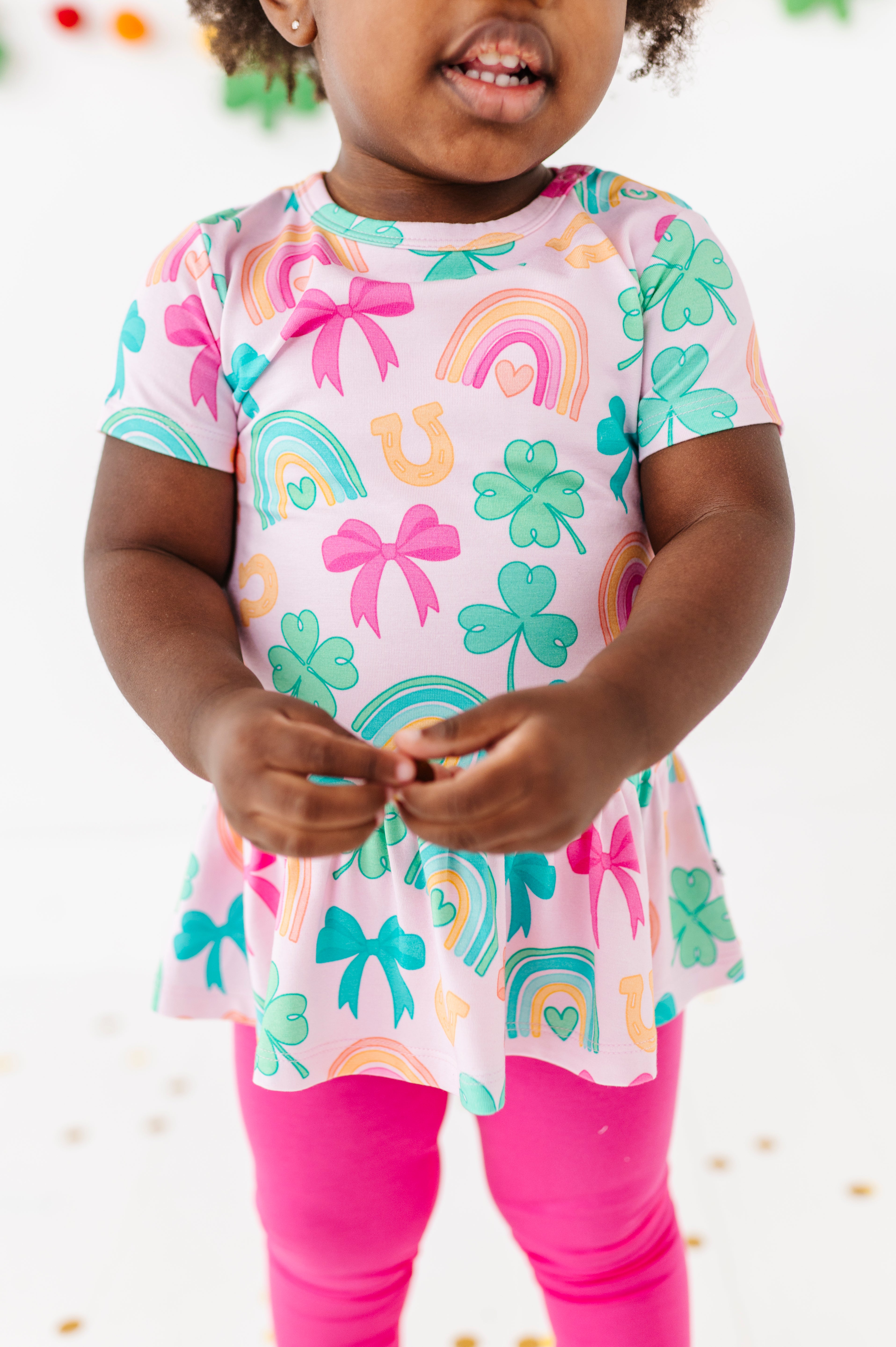 Close-up shot of a child wearing a lucky charm bamboo cotton peplum top with hot pink bamboo leggings 
