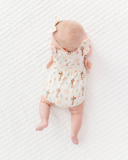 baby girl in a cross with florals bubble romper and a neutral colored headband on a white background 