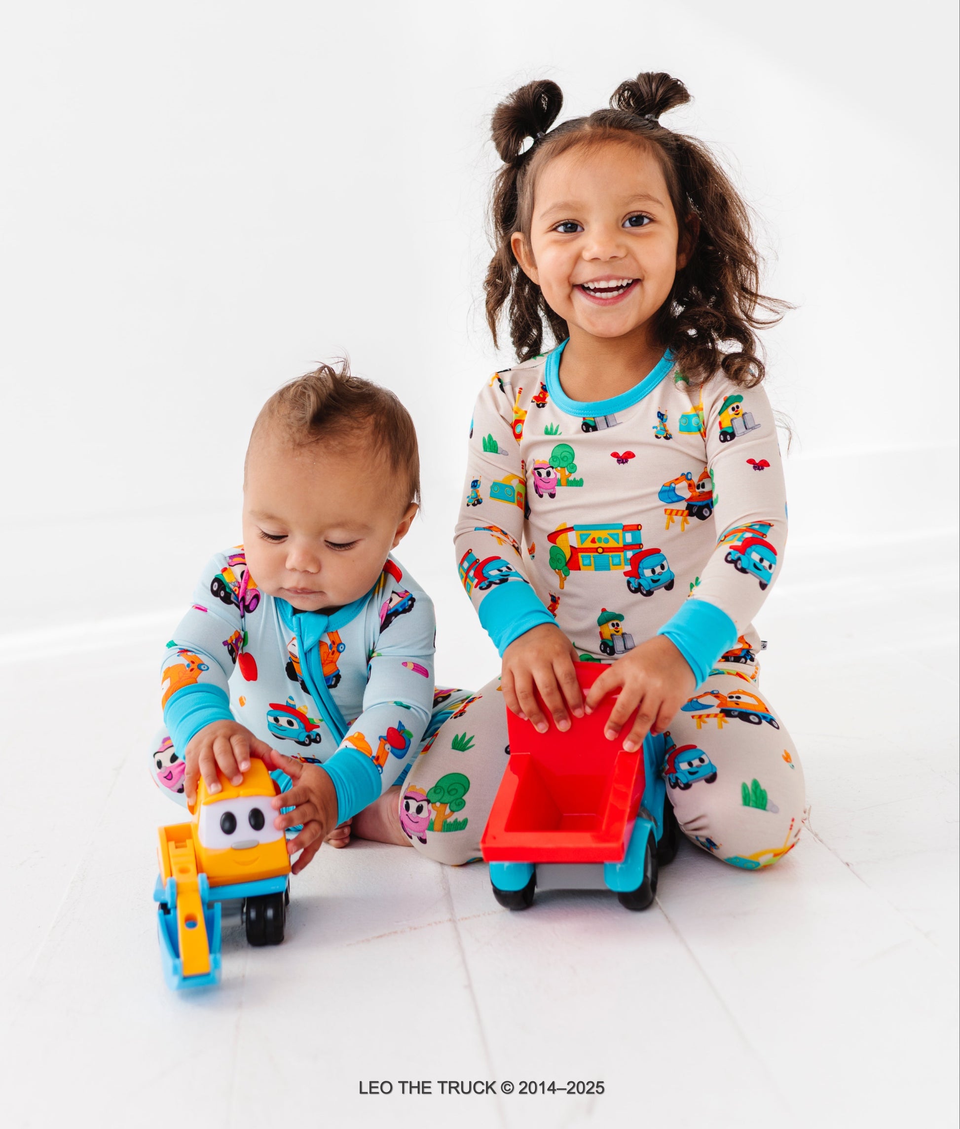 Siblings wearing coordinating Leo the Truck bamboo pajamas and playing with Leo the Truck and crew toys 