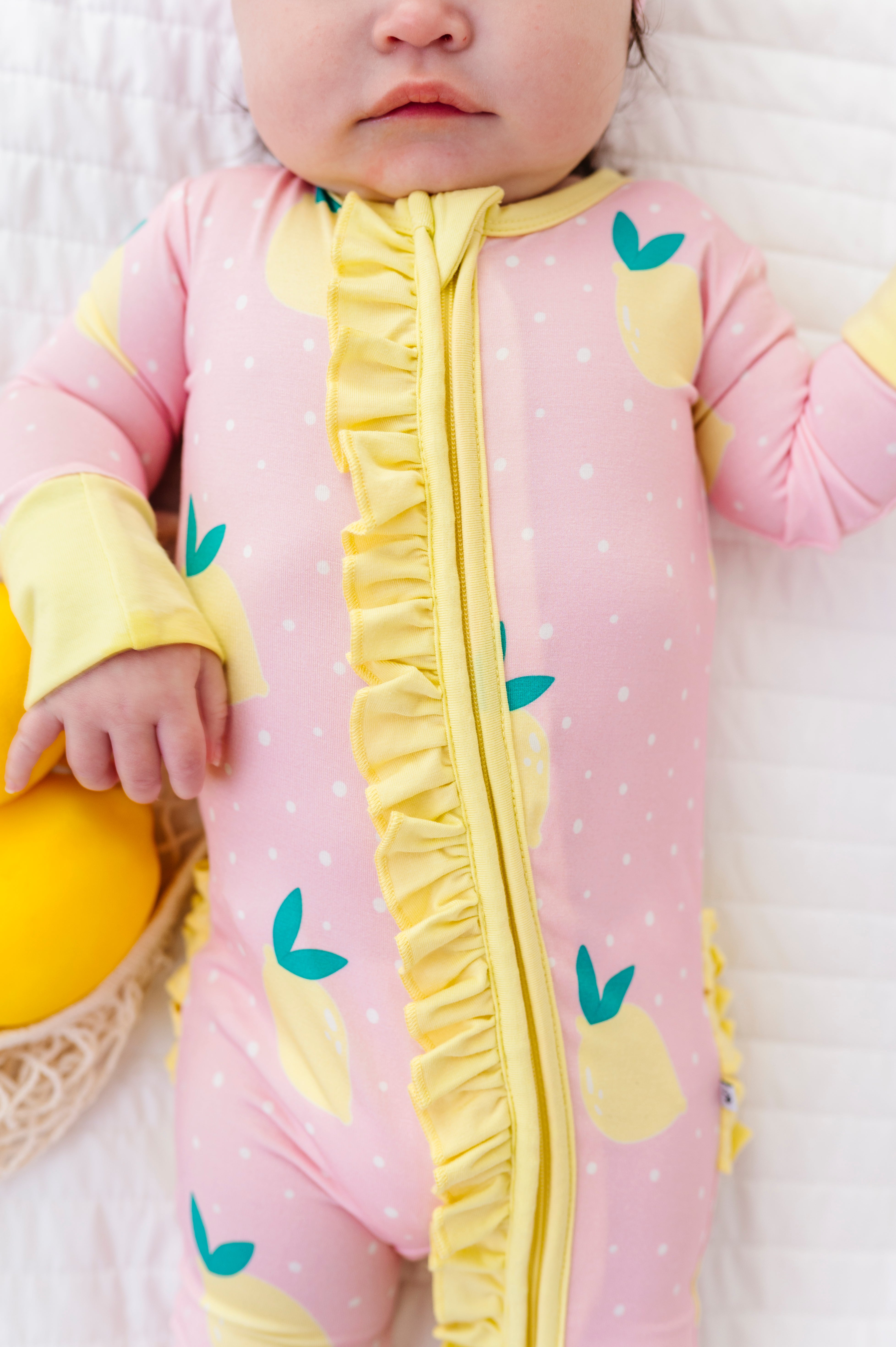 Baby wearing a pink and yellow romper with lemon designs on a white background
