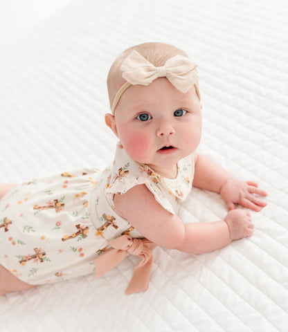 baby girl in a cross with florals bubble romper and a neutral colored headband on a white background 