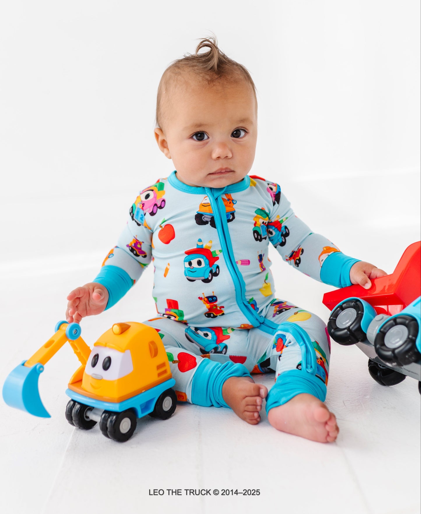 Baby boy in colorful Leo the Truck bamboo pajamas with toy Leo the Truck on a white background