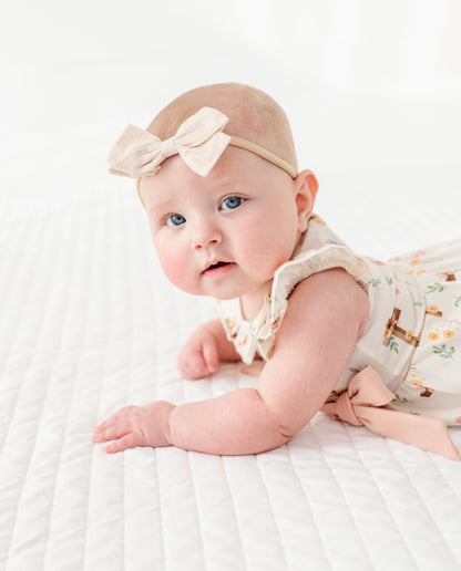 baby girl in a cross with florals bubble romper and a neutral colored headband on a white background 