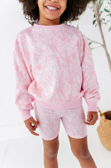 Child wearing a pink tree camo outfit with a neutral background