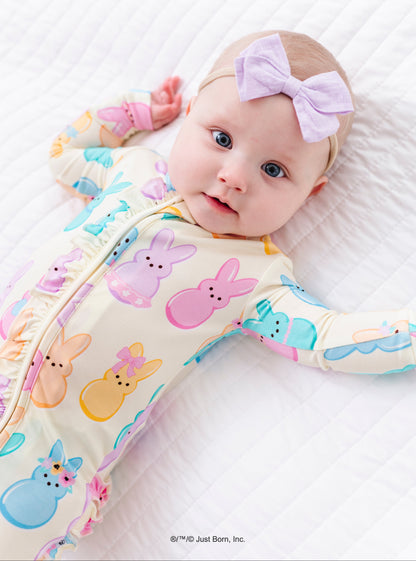 Baby wearing a colorful romper with PEEPS® bunny pattern and a headband on a white background