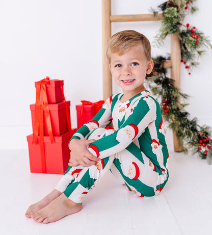 A young blonde boy wearing green-and-beige striped bamboo pajamas with Santa faces all over them. The super soft bamboo pajamas are ribbed and made to fit snugly for safety standards. The boy is sitting in front of 5 red-wrapped presents 