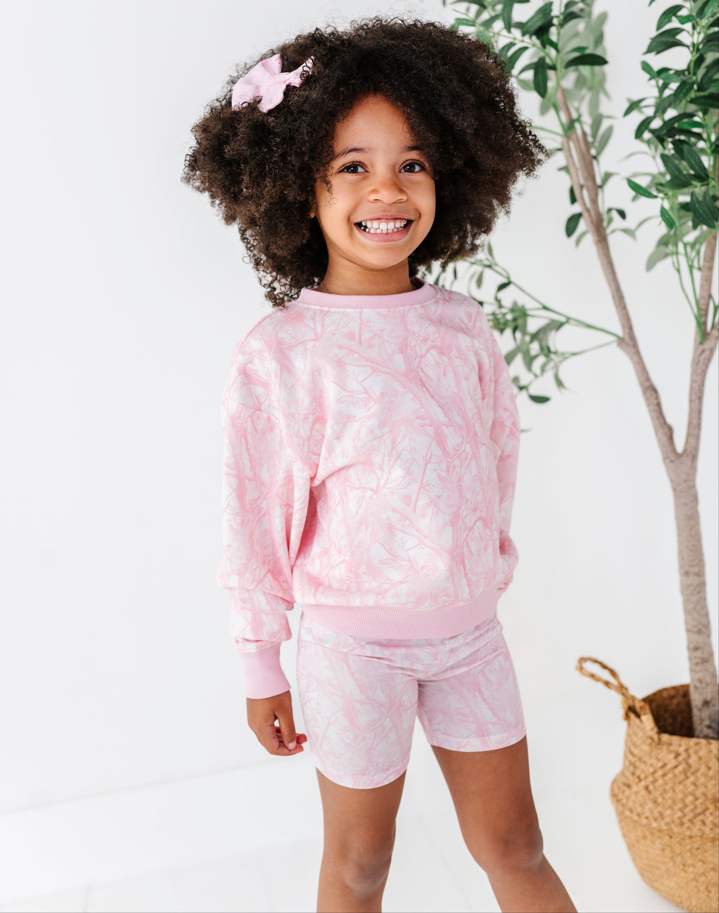 Young girl wearing a pink camo outfit with a plant in the background
