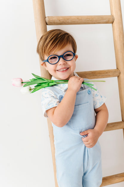 Child wearing glasses holding tulips standing next to a wooden ladder on a white background