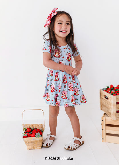 Young girl in a Strawberry Shortcake™ dress standing next to strawberry-themed props on a white background