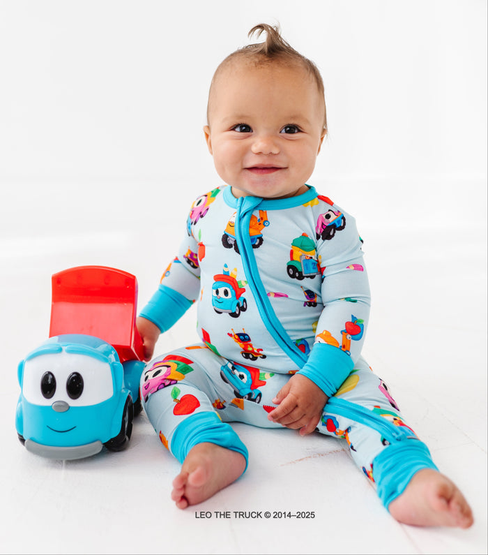 Baby wearing a colorful Leo the Truck zip romper, sitting next to a toy Leo the Truck on a white background.
