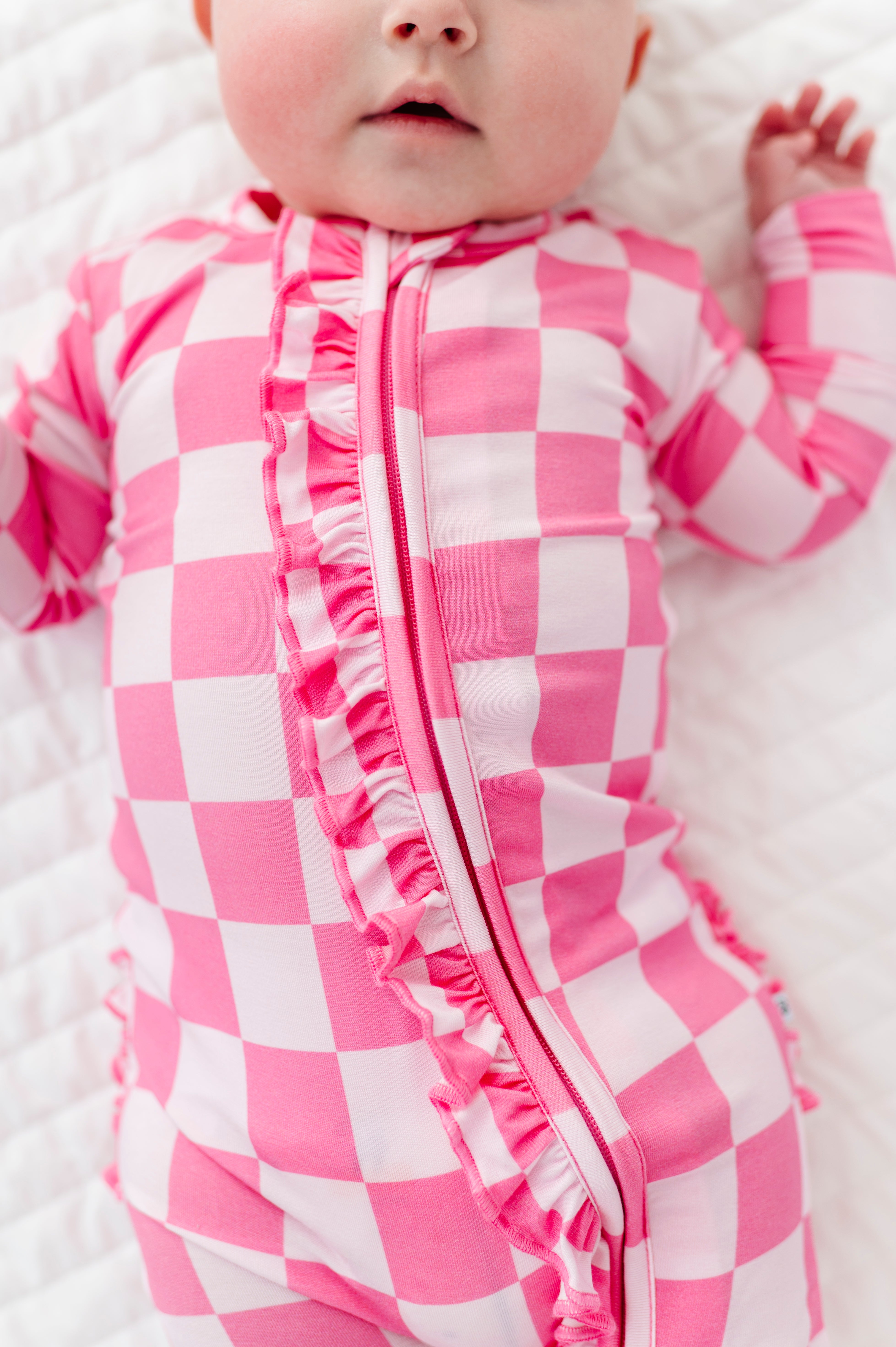 Baby wearing a pink and white checkered bamboo onesie on a white blanket
