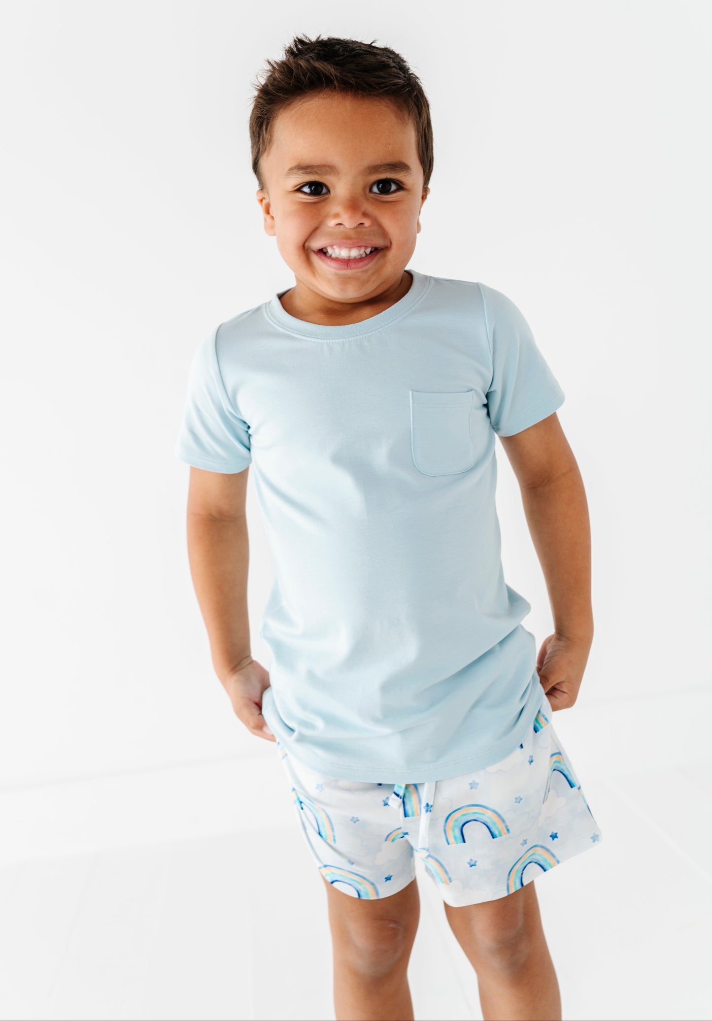 Child wearing a light blue t-shirt and patterned shorts on a white background