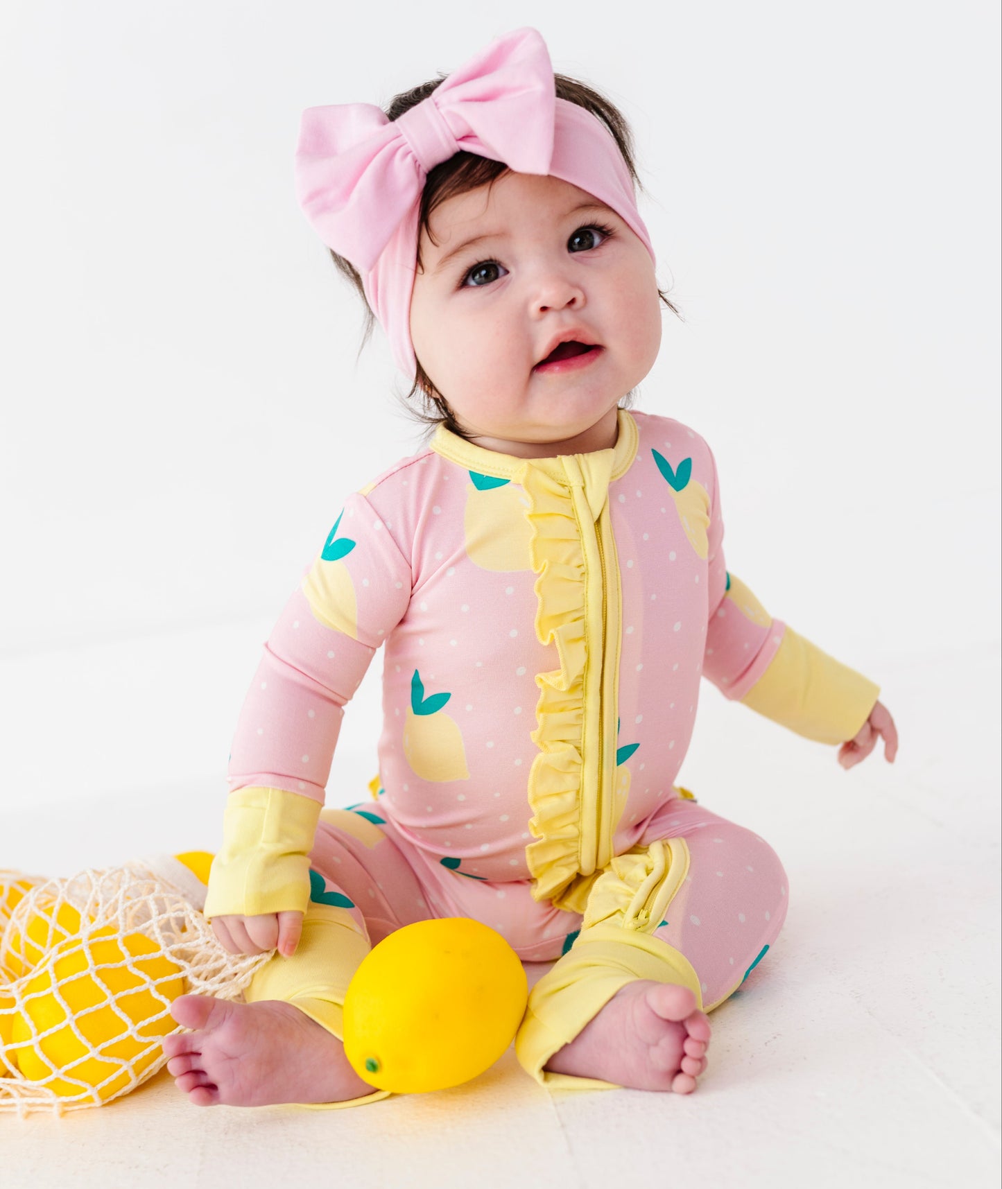 Baby in a pink and yellow ROMPER with a large bow on a white background