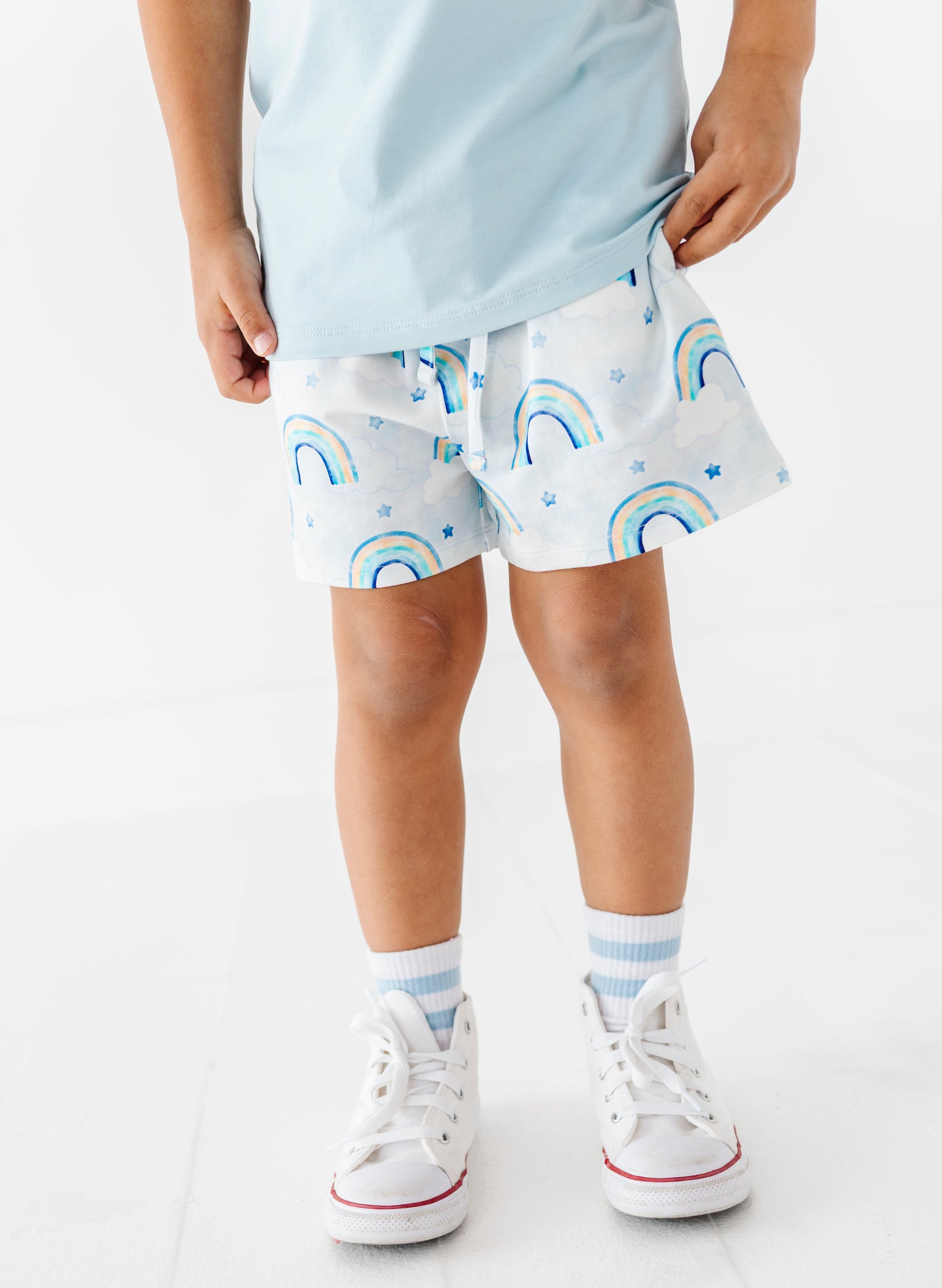 Child wearing light blue bamboo cotton shorts with watercolor rainbow pattern on a white background