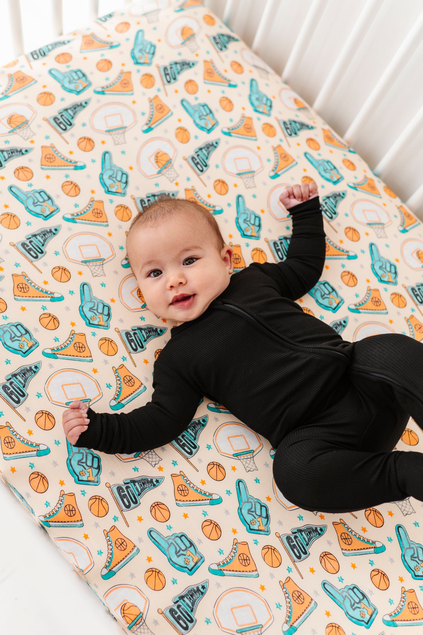 Baby lying on a bamboo crib sheet with sports-themed designs