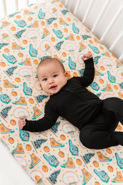 Baby lying on a bamboo crib sheet with sports-themed designs