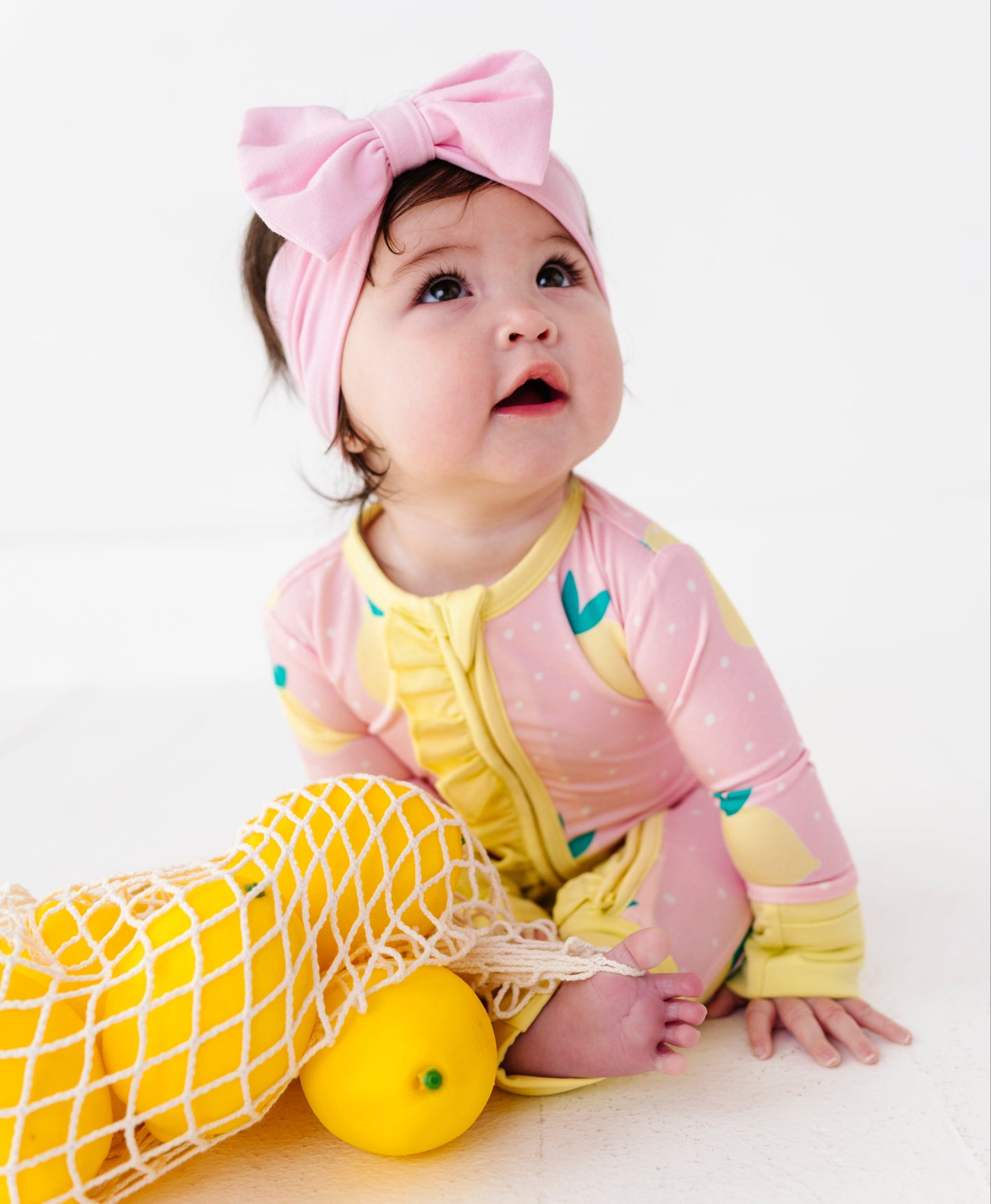 Baby in pink and yellow romper with a bag of lemons on a white background