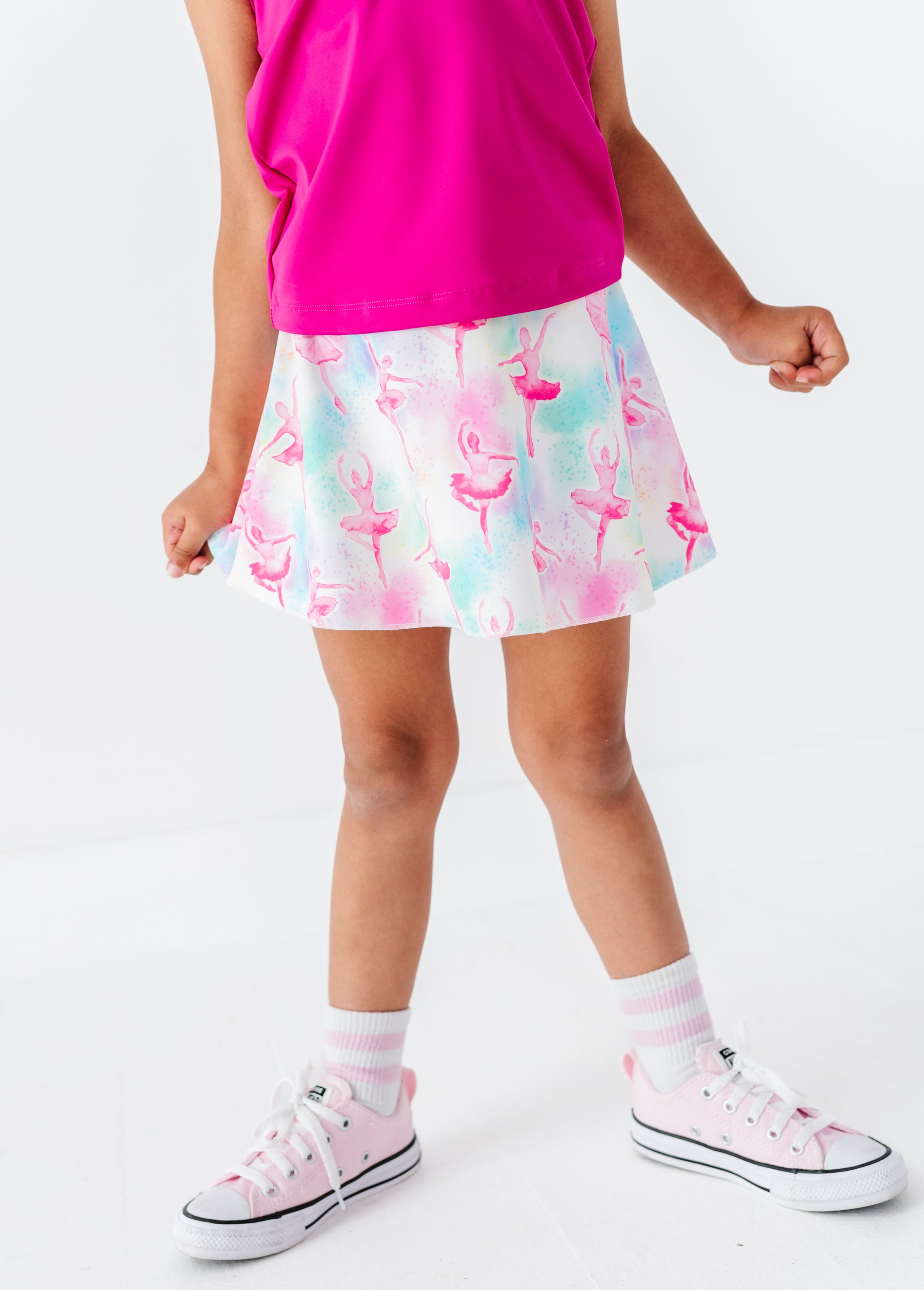 Girl wearing a pink top, colorful skirt, and white sneakers on a white background