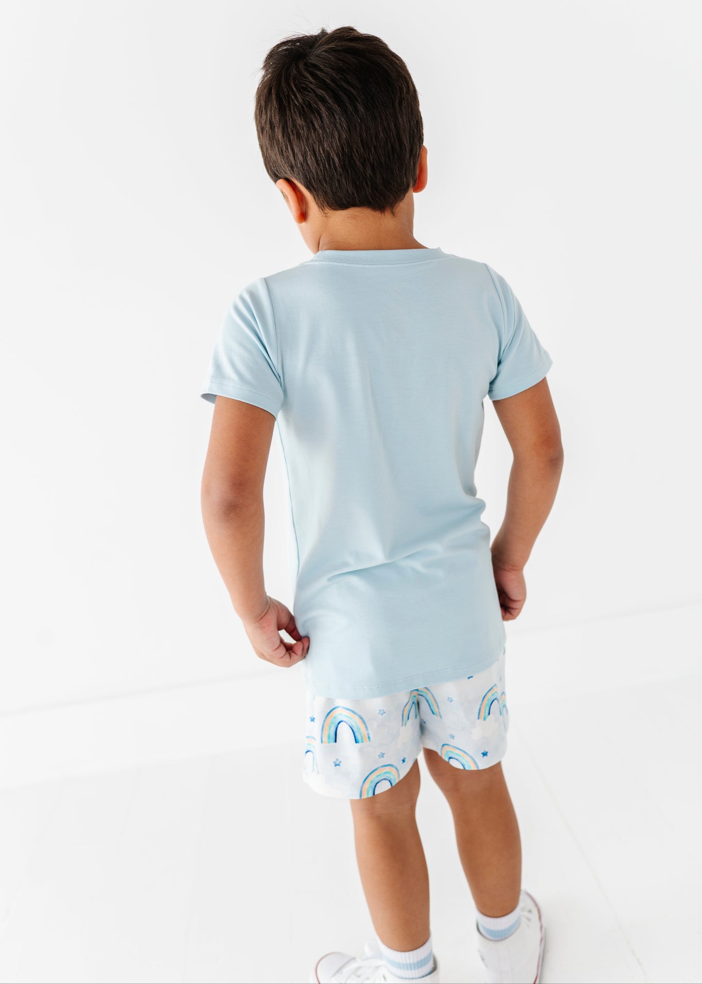 Child wearing a light blue t-shirt and patterned shorts on a white background