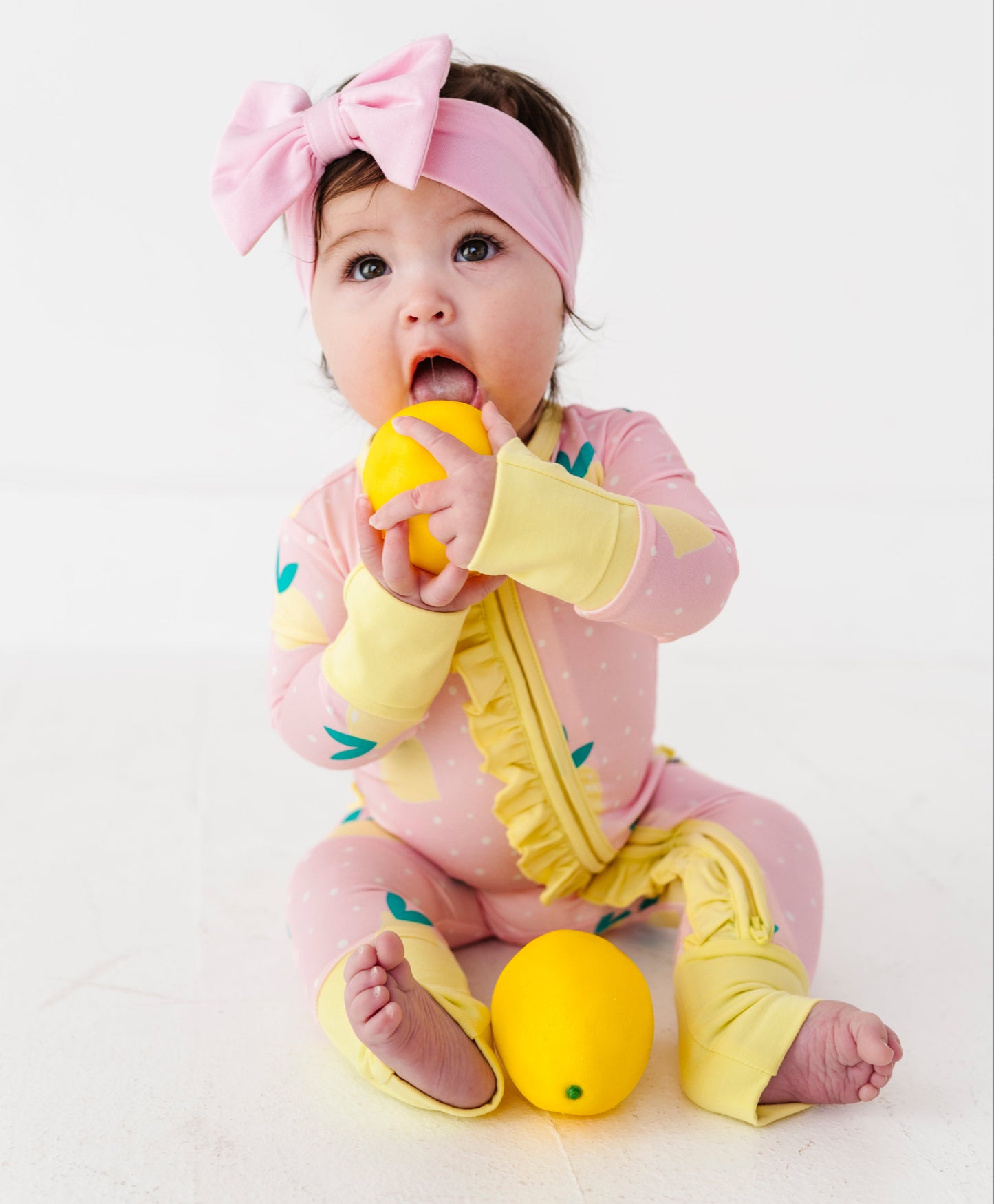 Baby in pink and yellow romper with a lemon toy on a white background