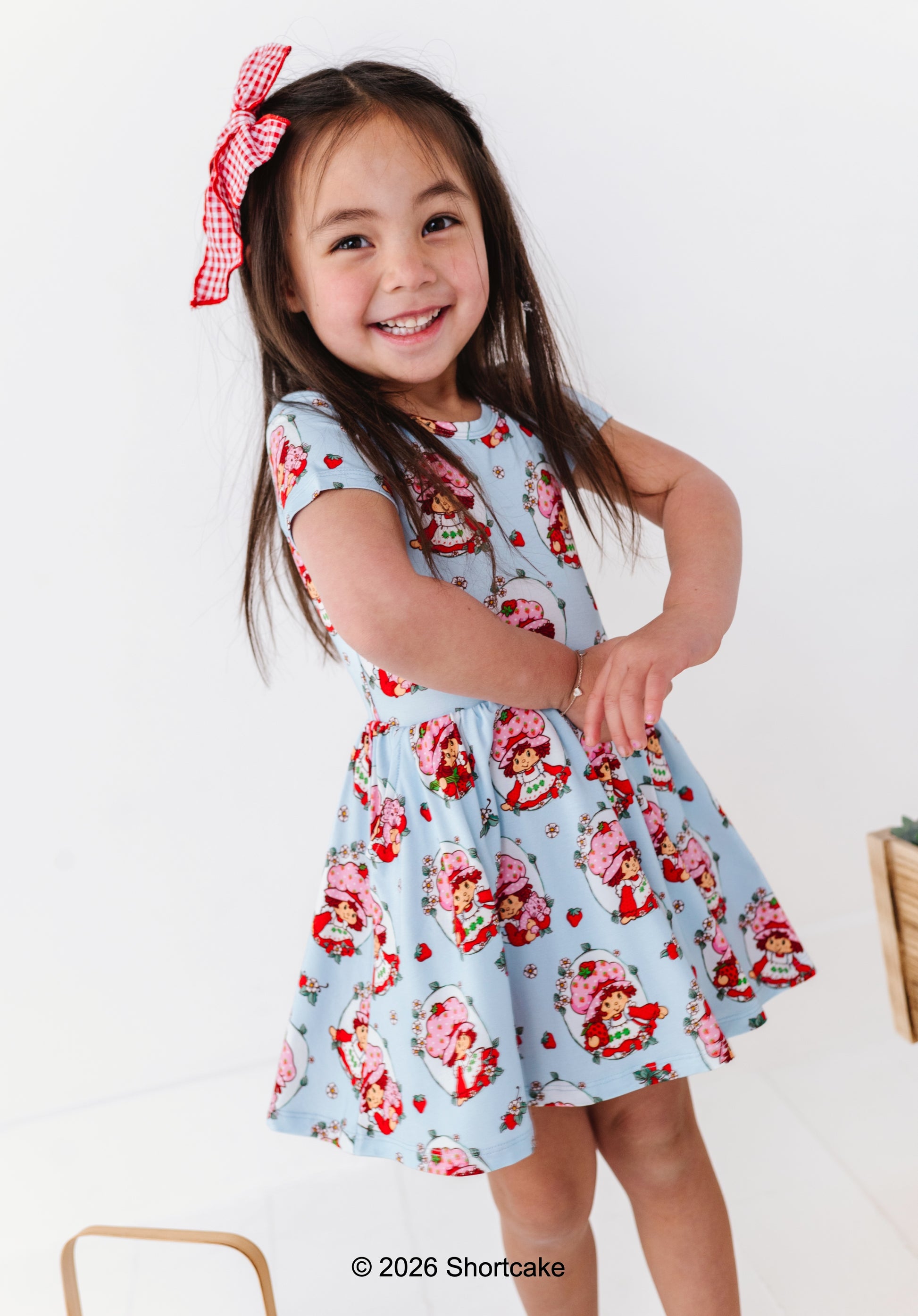 Young girl wearing a Strawberry Shortcake™ dress with a red bow on a white background