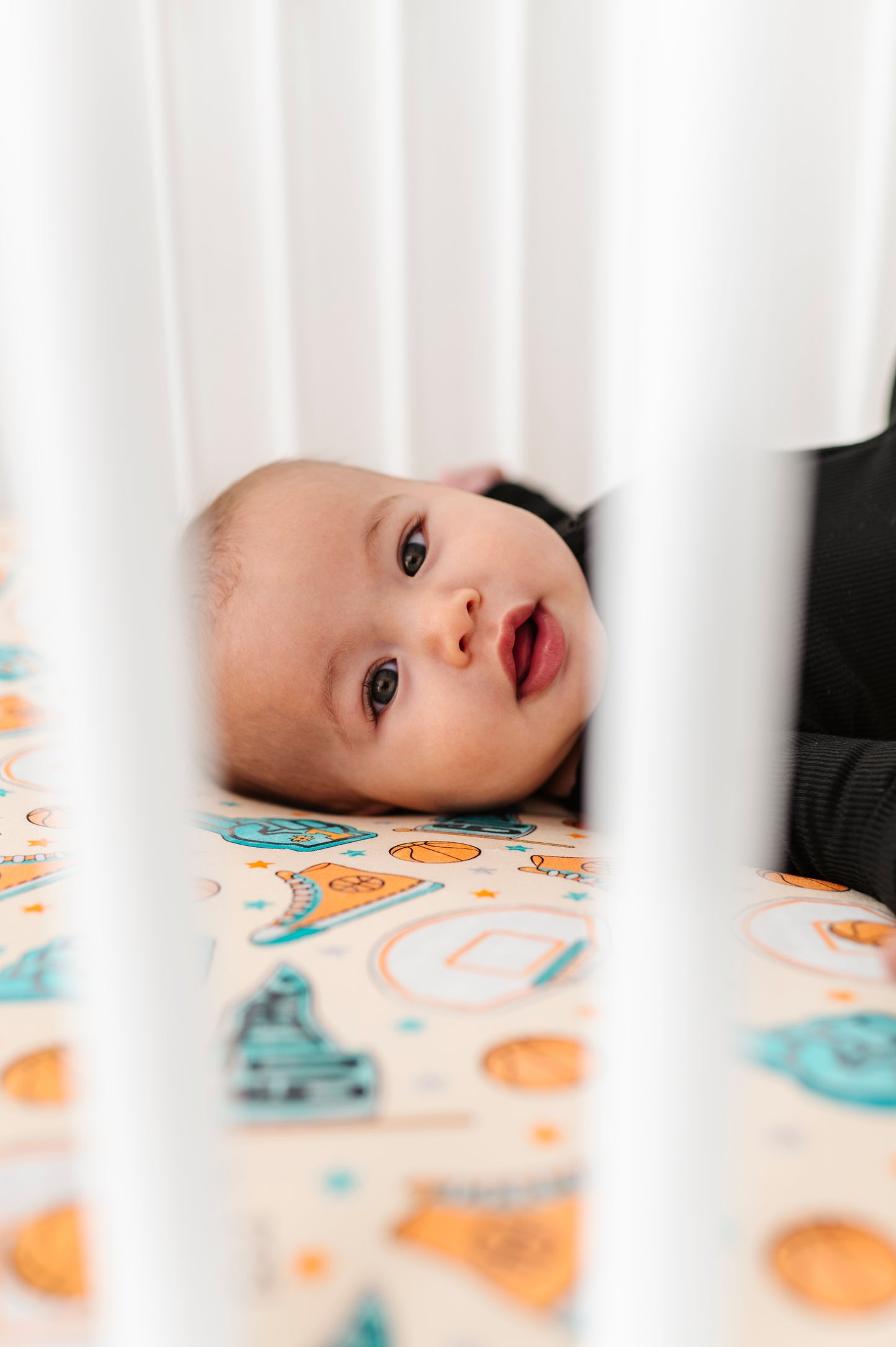 Baby lying in a crib with a sports themed sheet