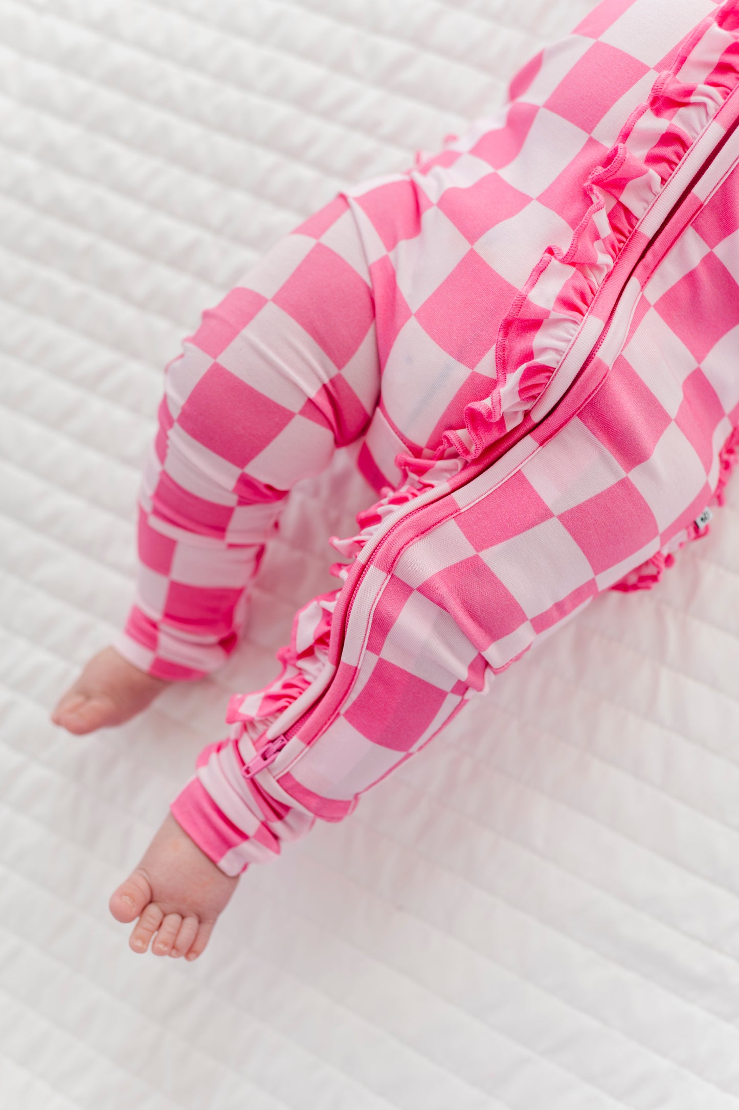 Baby in pink checkered bamboo romper lying on a white textured surface