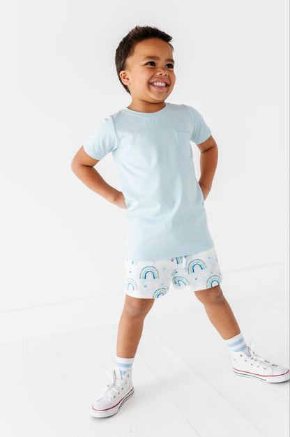 Child wearing a light blue t-shirt and patterned shorts on a white background