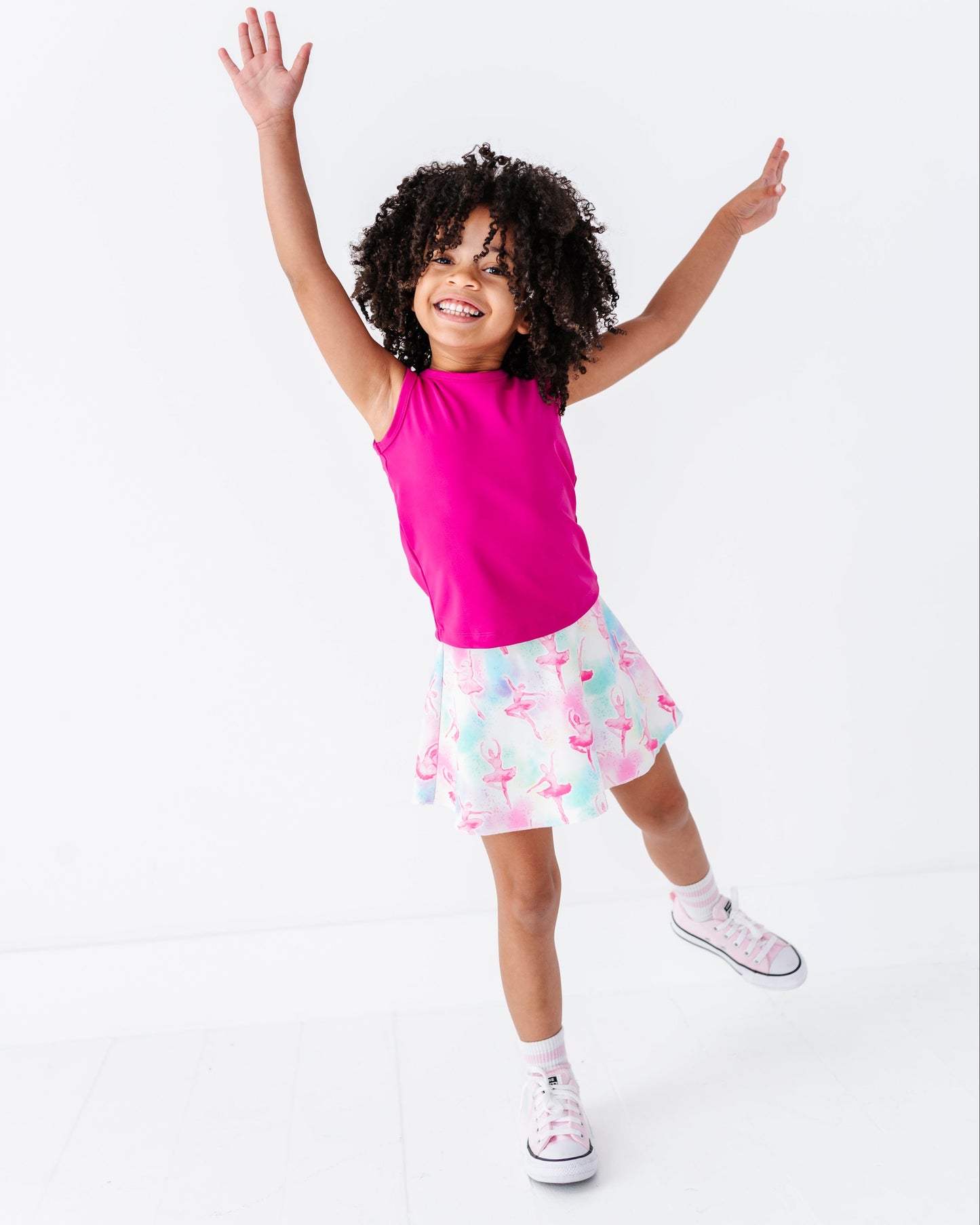 Child wearing a pink top and patterned skirt with arms raised on a white background