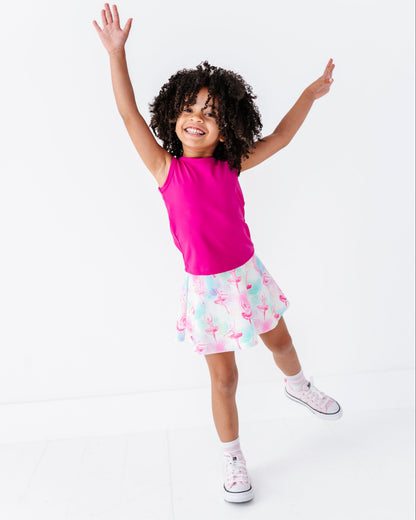 Child wearing a pink top and patterned skirt with arms raised on a white background