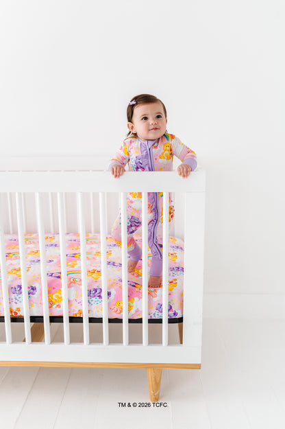 Baby standing on a crib with colorful Care Bears™ bedding against a white background