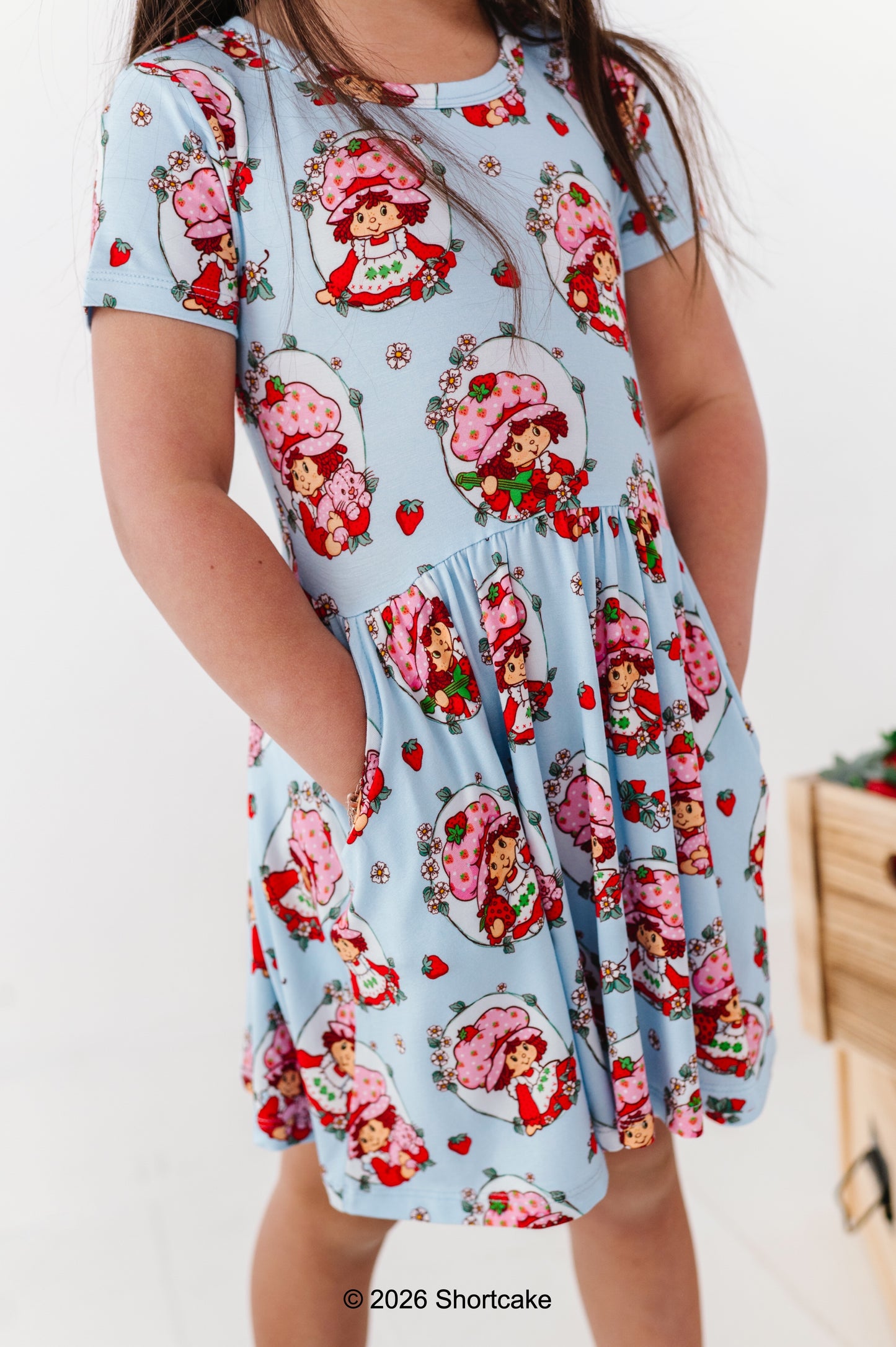 Child wearing a dress with Strawberry Shortcake™ print on a light blue background