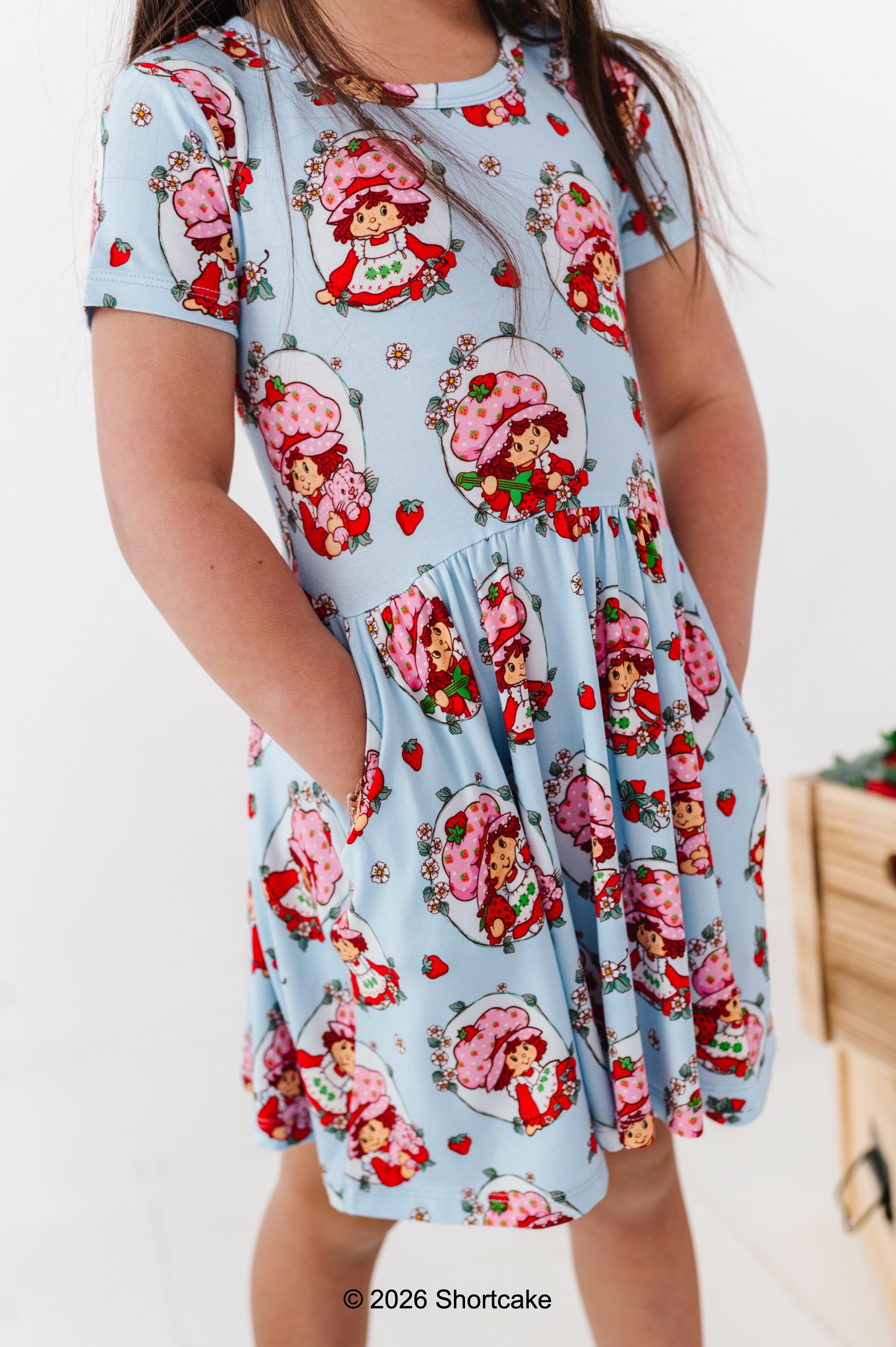 Child wearing a dress with Strawberry Shortcake™ print on a light blue background