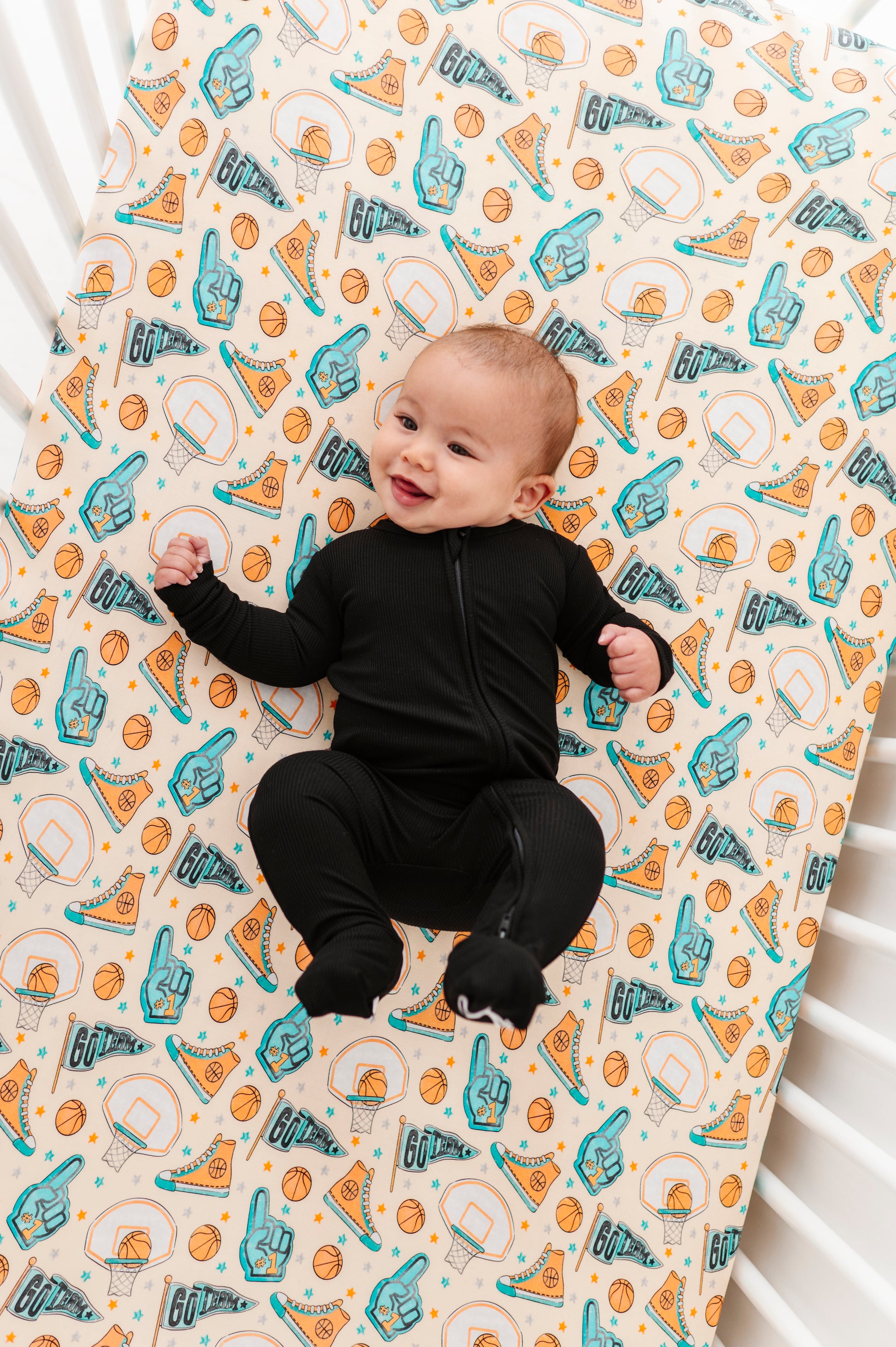 Baby lying on a crib with a patterned bamboo sheet featuring sports-themed designs.