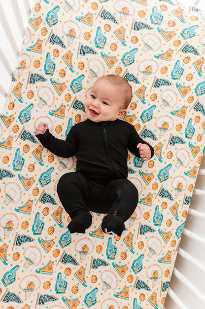 Baby lying on a crib with a patterned bamboo sheet featuring sports-themed designs.