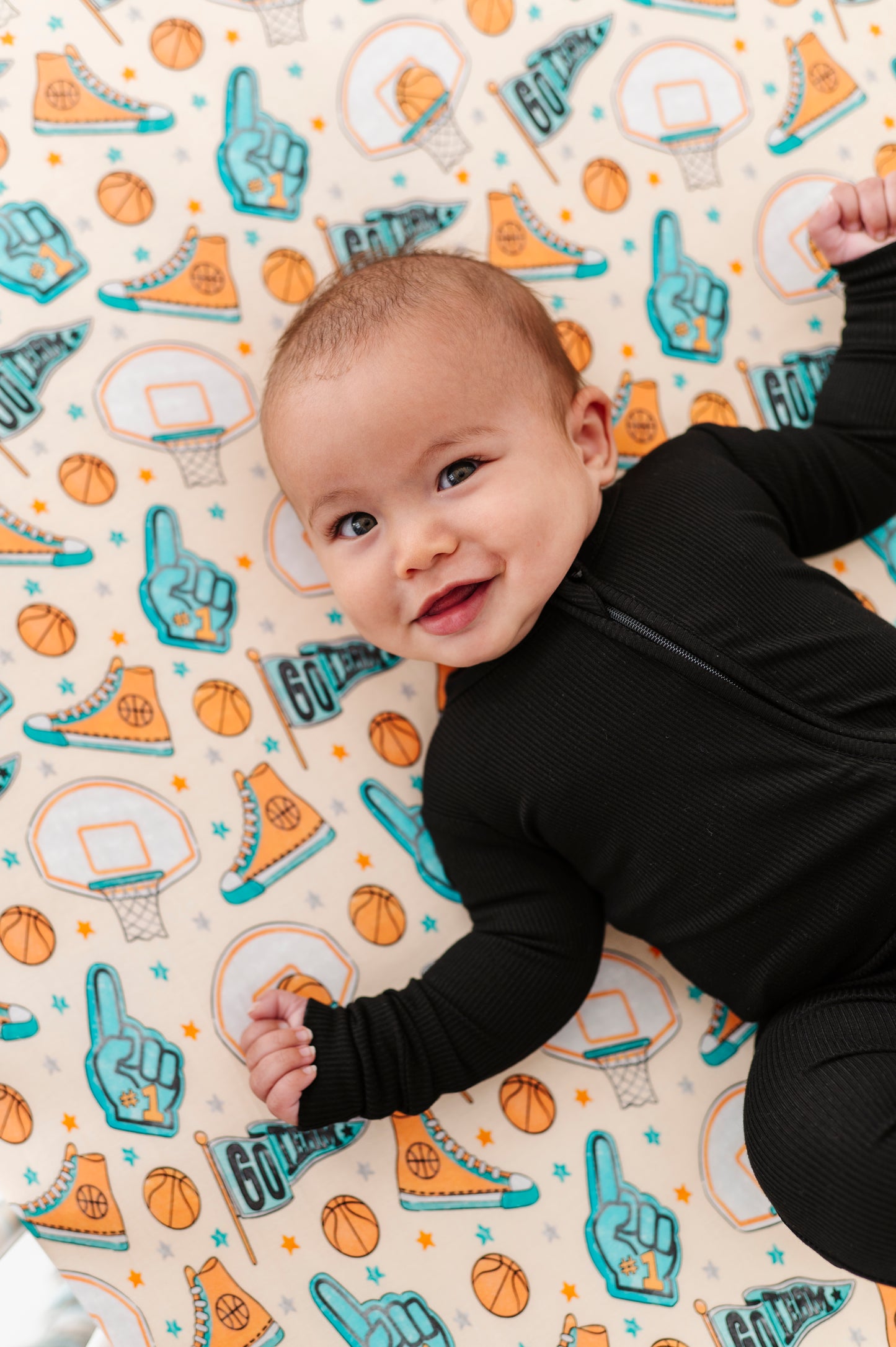 Baby lying on a colorful bamboo crib sheet with sports-themed designs