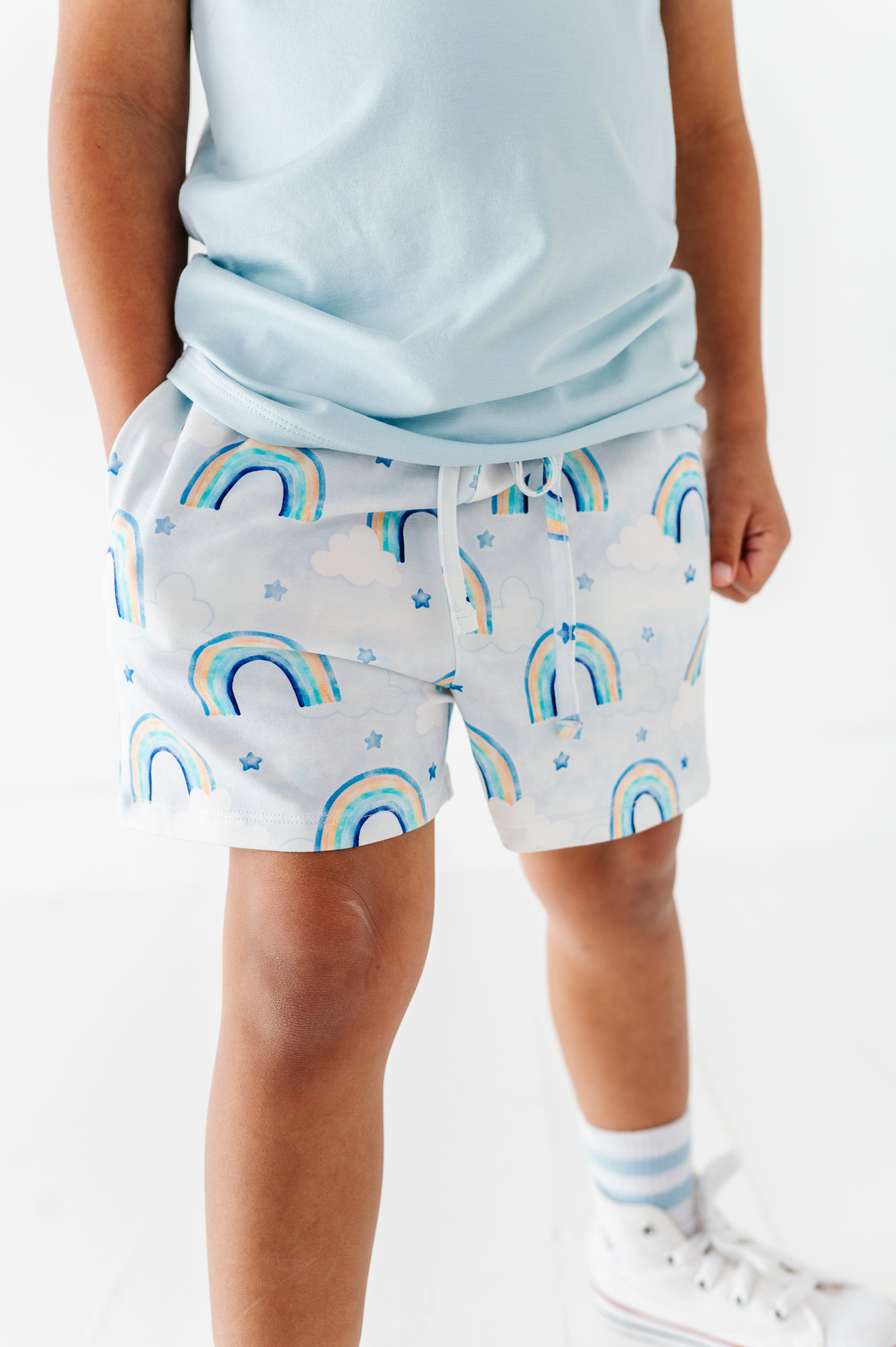 Child wearing light blue shorts with rainbow pattern on a white background