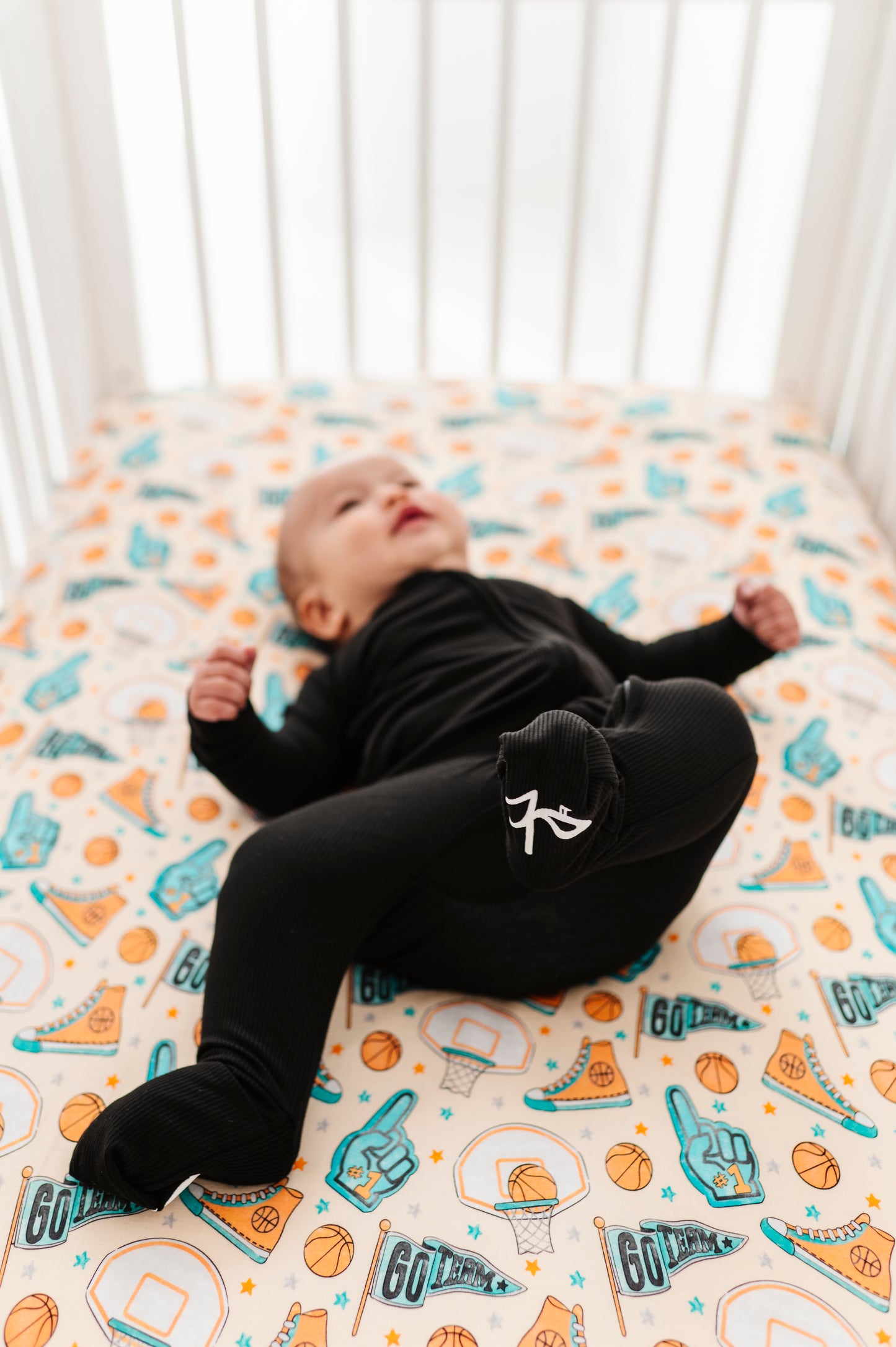 Baby lying on a bamboo crib sheet with sports-themed design