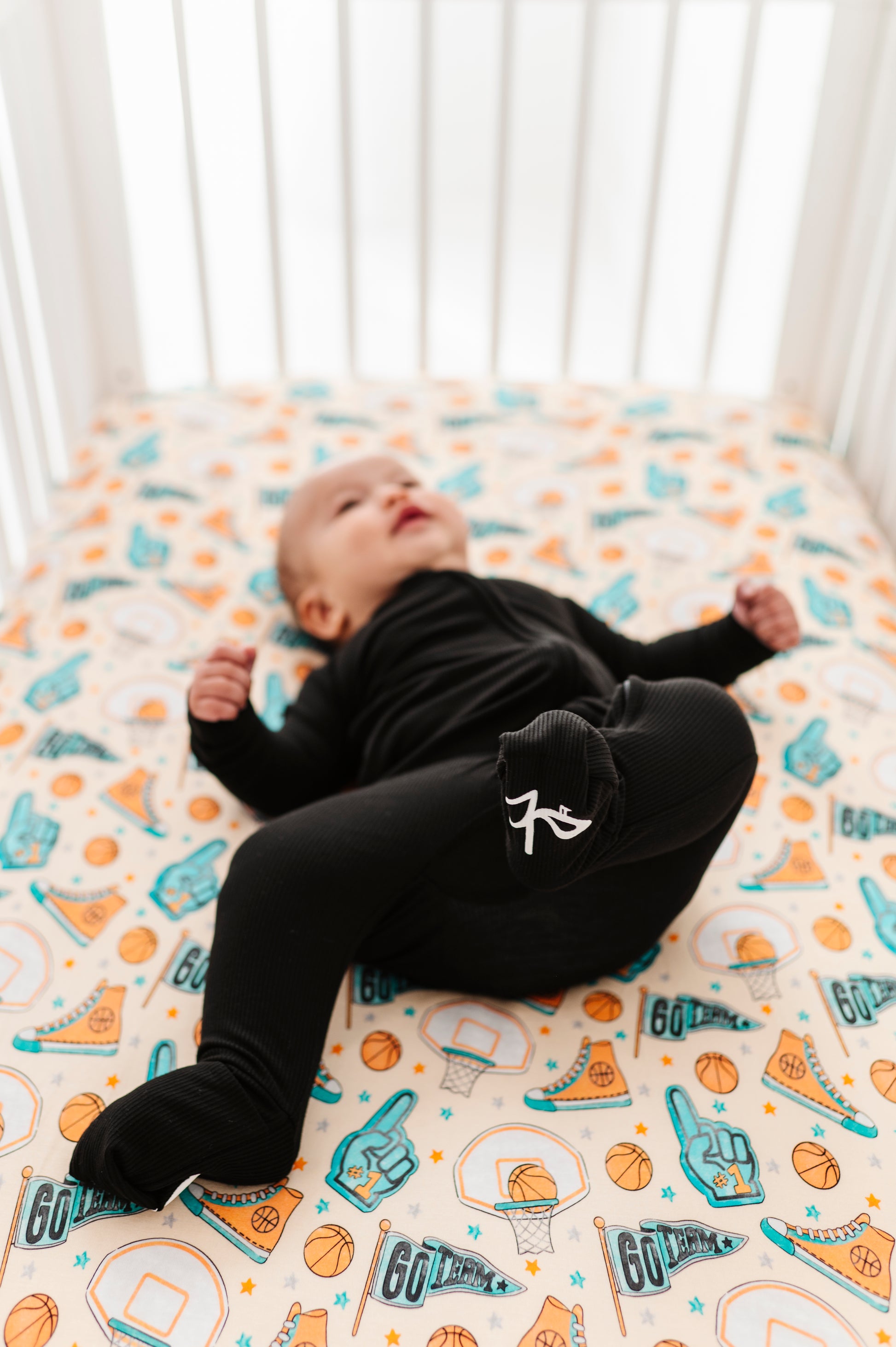 Baby lying on a bamboo crib sheet with sports-themed design