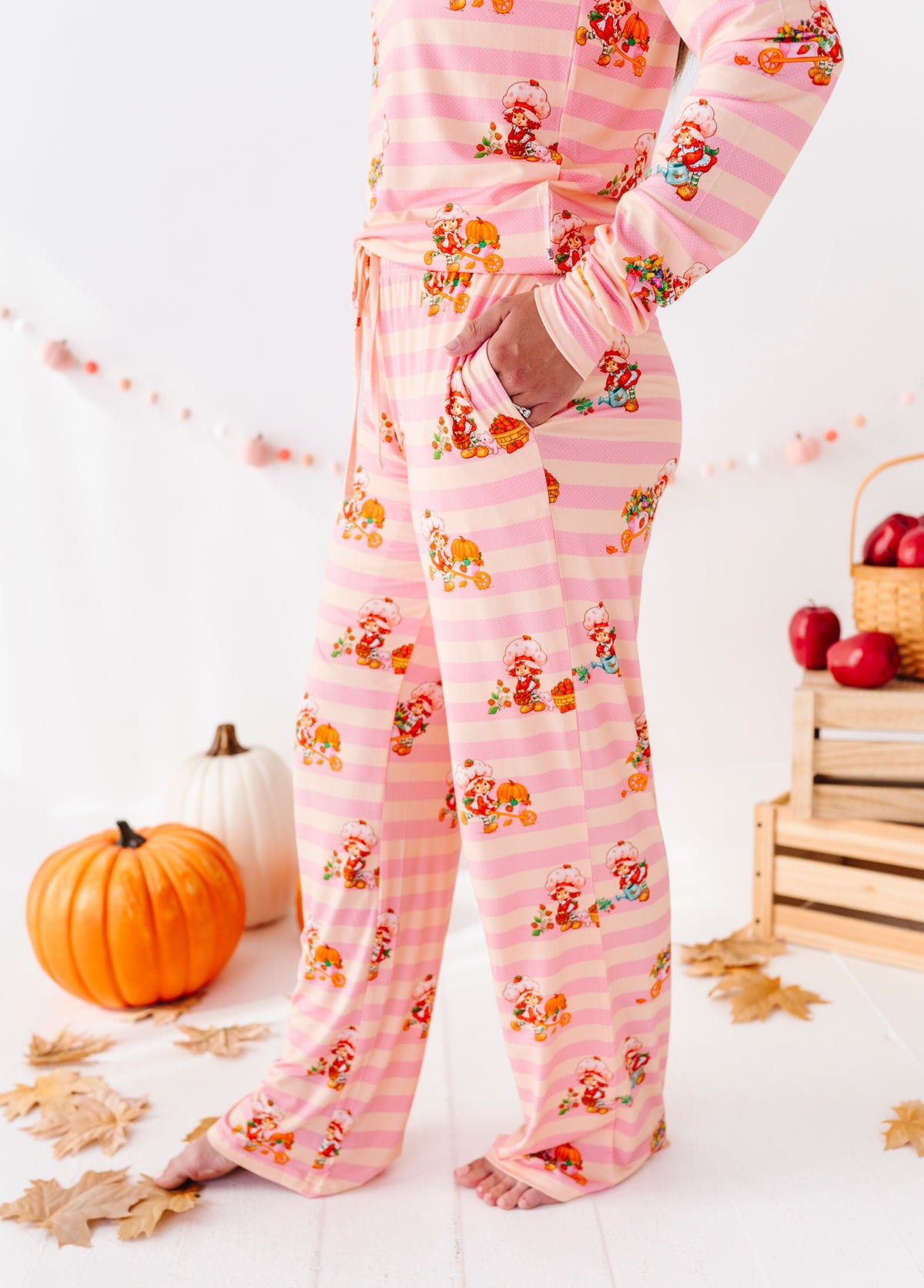 Pink striped pajama pants with a Santa Claus and turkey print, shown on a model in a fall-themed room setting with pumpkins and autumn leaves.
