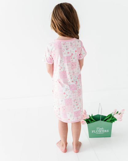 Child wearing a pink floral bamboo gown standing next to a green bucket of flowers on a white background