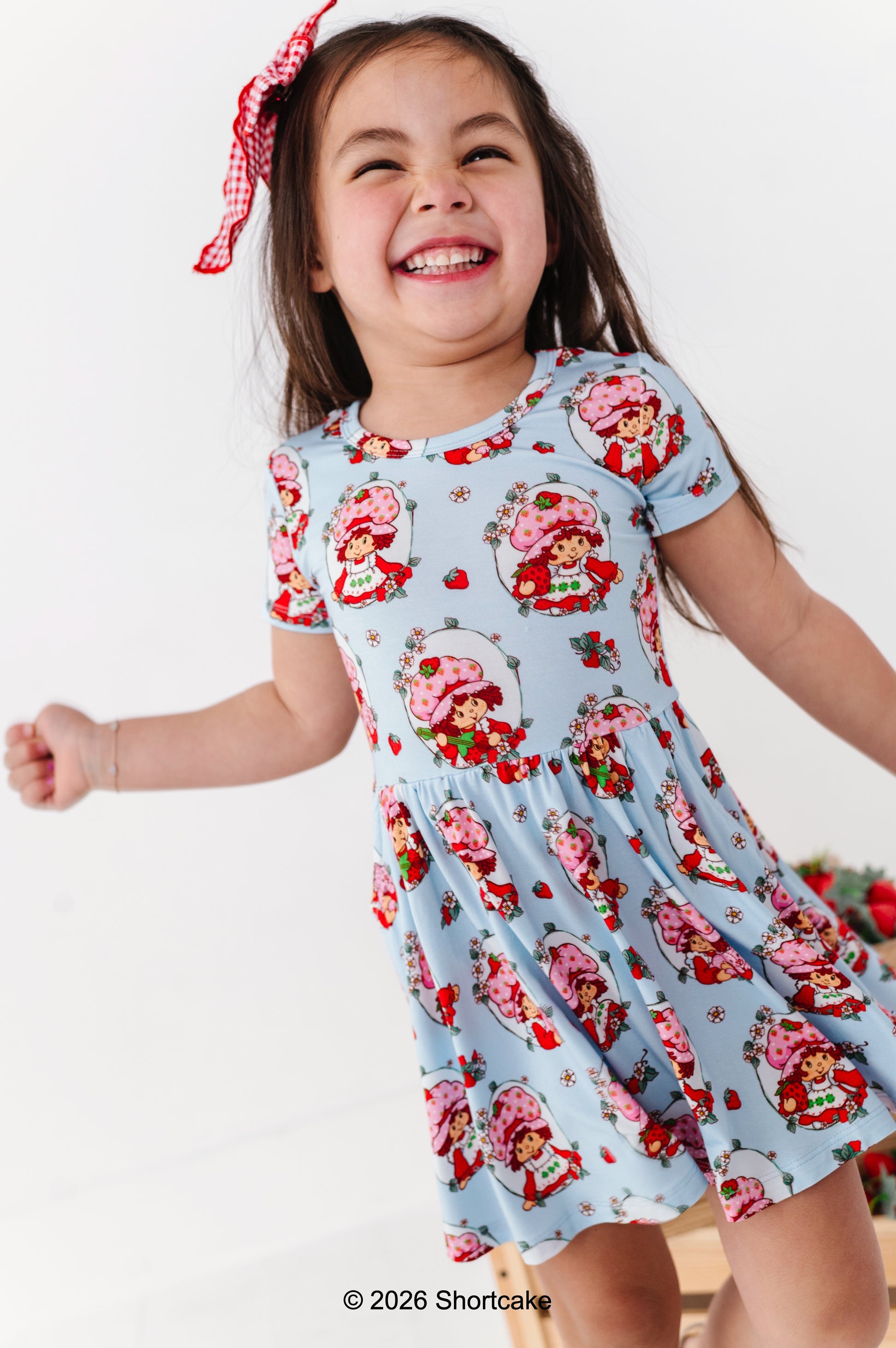 Child wearing a light blue dress with Strawberry Shortcake™ print on a white background