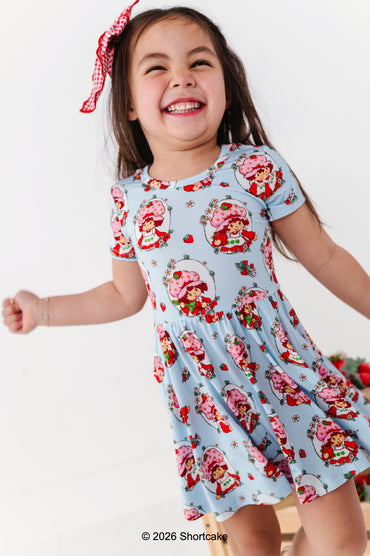 Child wearing a light blue dress with Strawberry Shortcake™ print on a white background