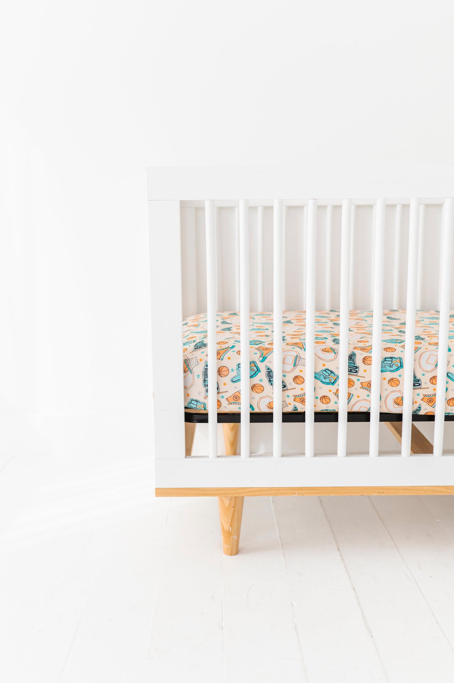 White crib with a basketball themed bamboo crib sheet on a white background