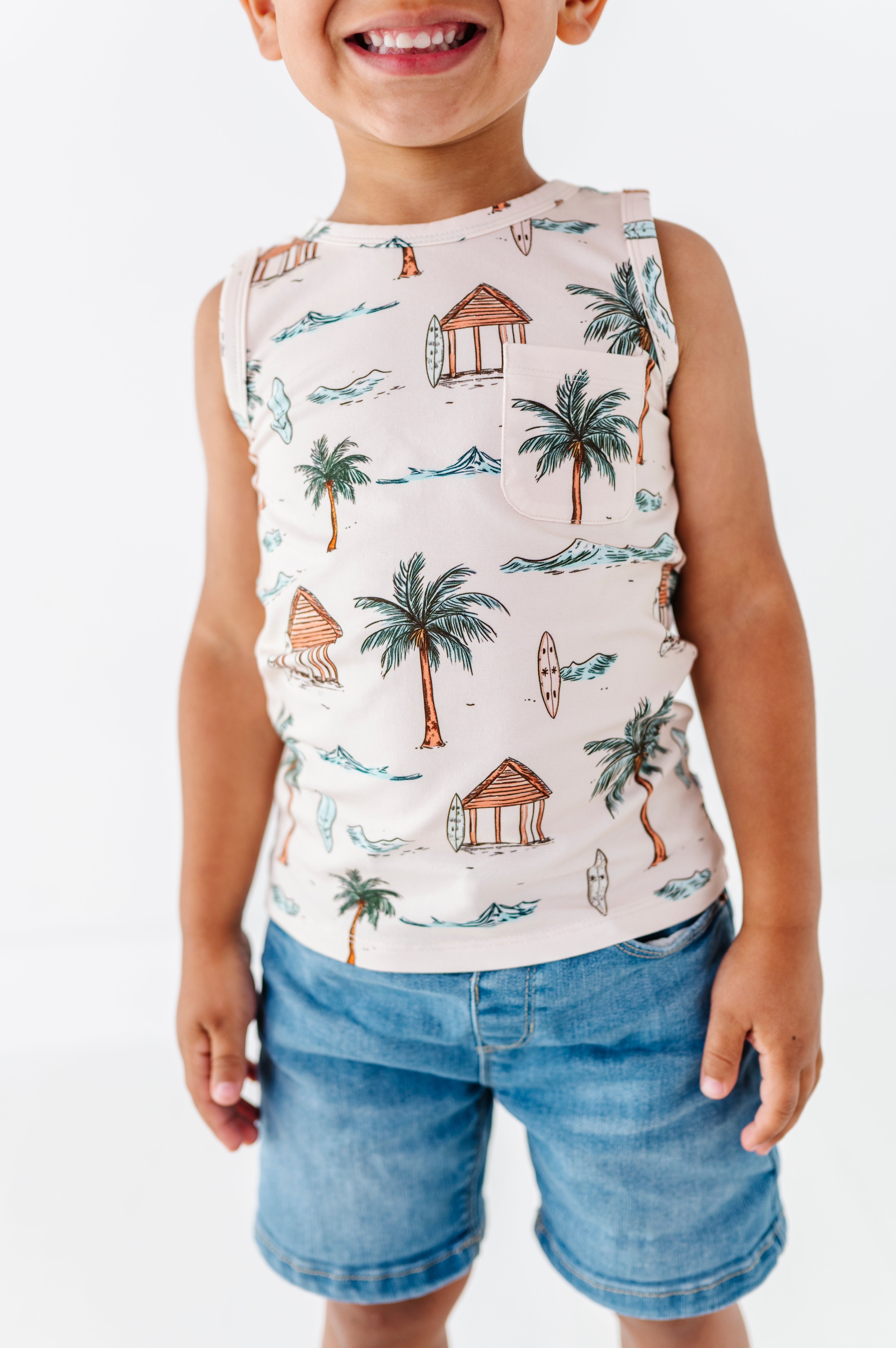 Child wearing a sleeveless shirt with a tropical pattern and denim shorts on a white background